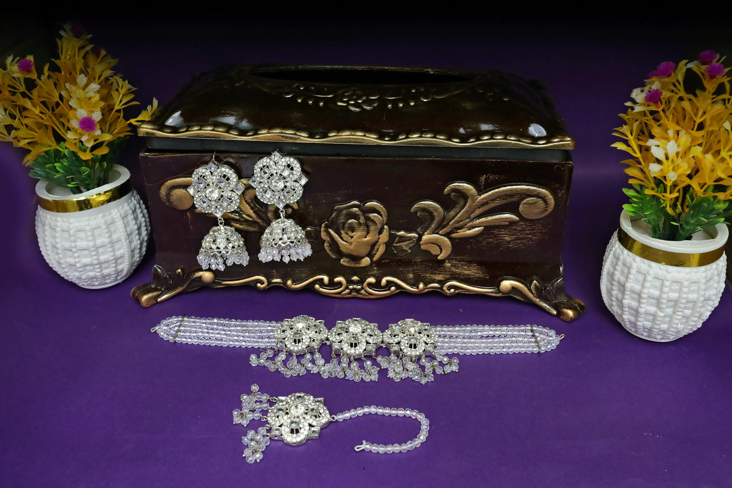 Decorative jewelry box with earrings, necklace, and bracelet on a purple surface with floral decorations.