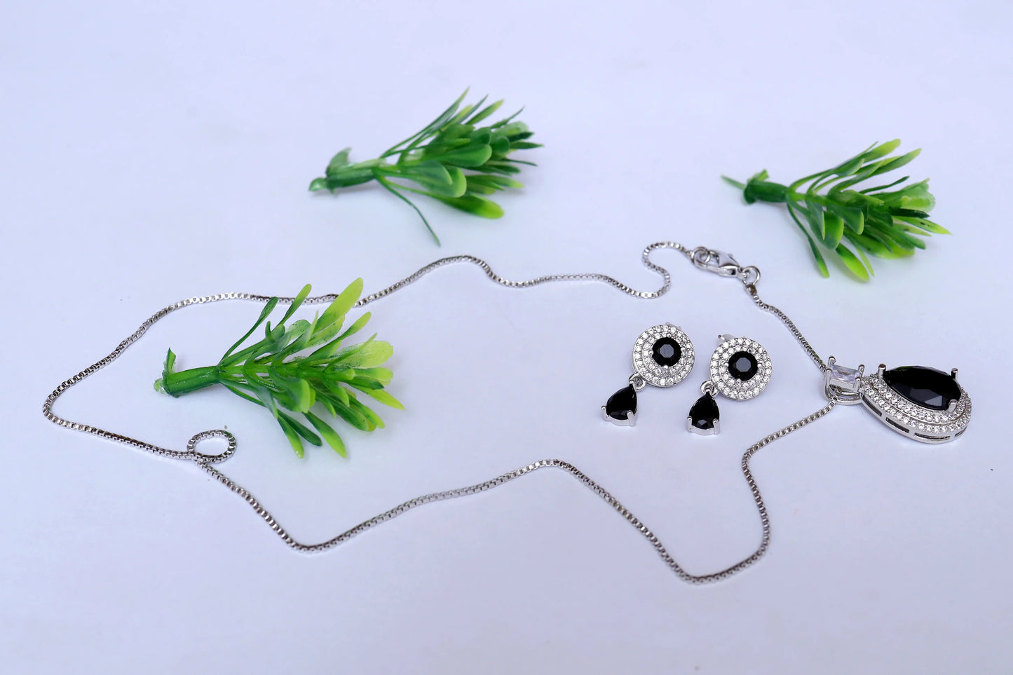 Jewelry set with necklace and earrings on a white background with green plants.