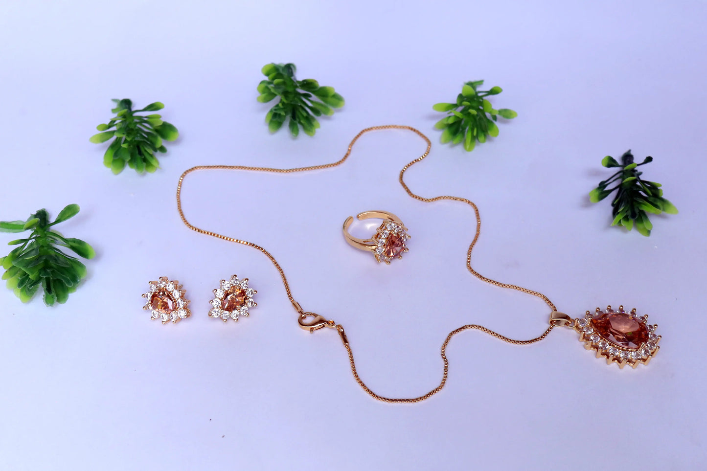 Pendent set with necklace, ring, and earrings on a white background with green leaves.