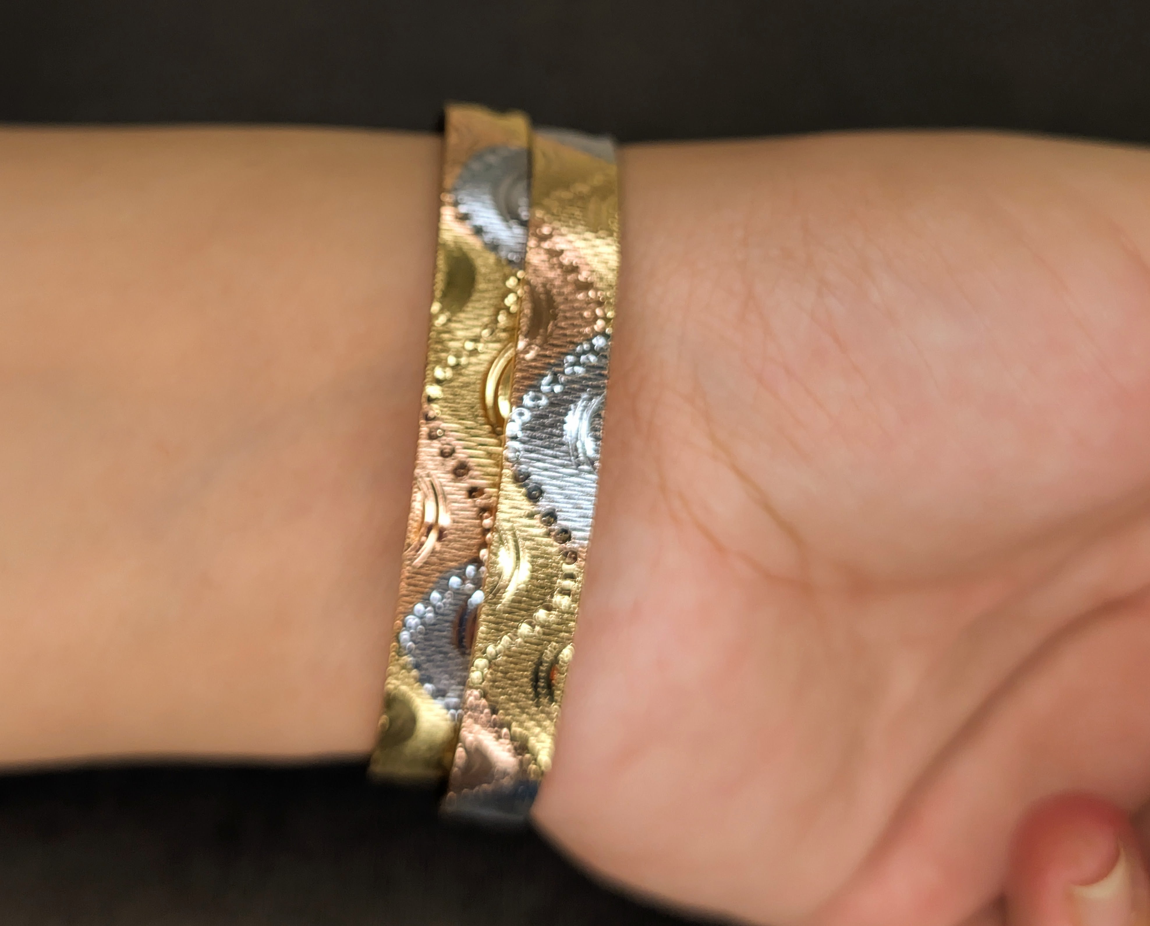 Close-up of a wrist wearing a gold and silver patterned bracelet.