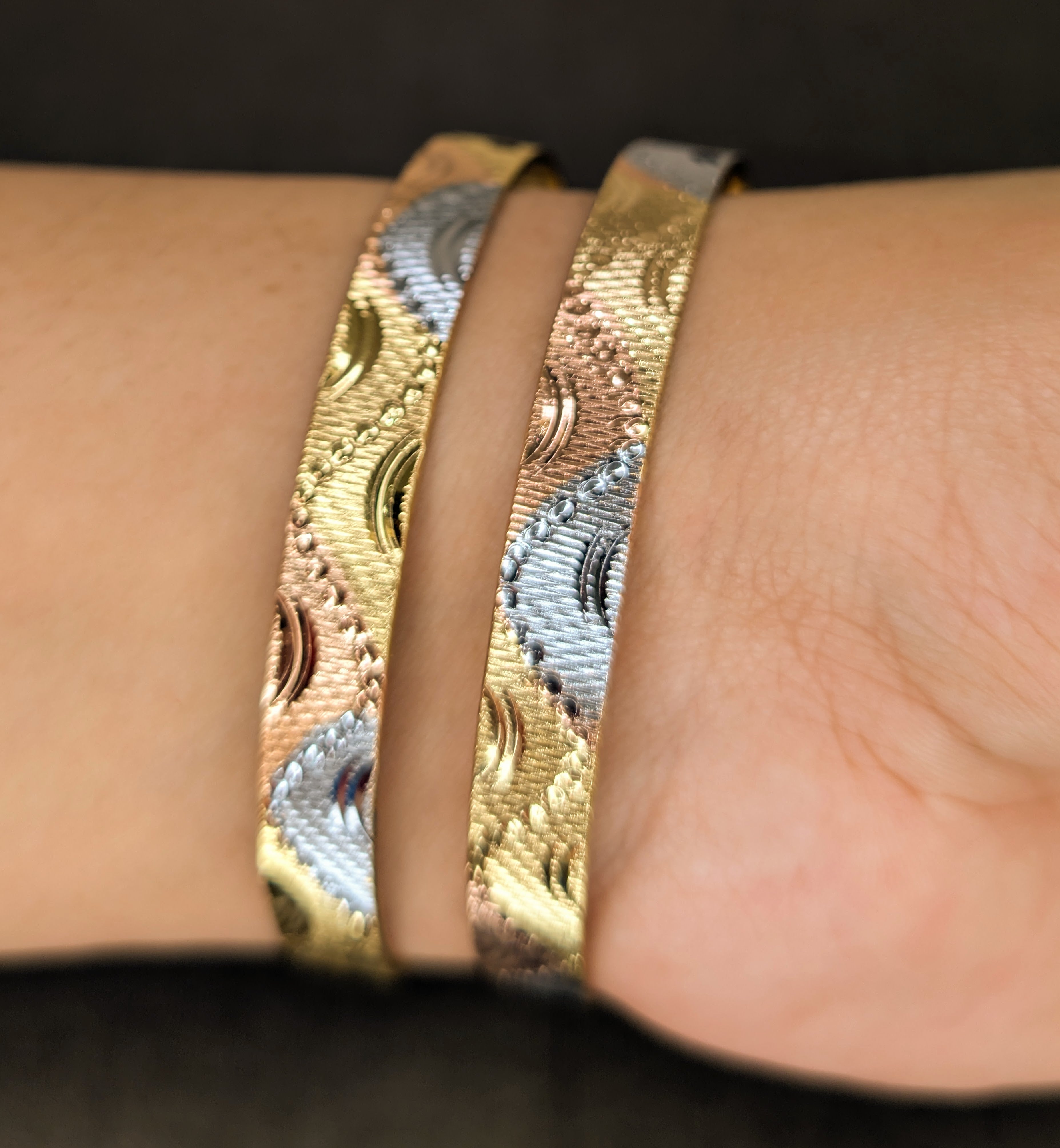 Close-up of a wrist wearing two gold bracelets with intricate patterns.