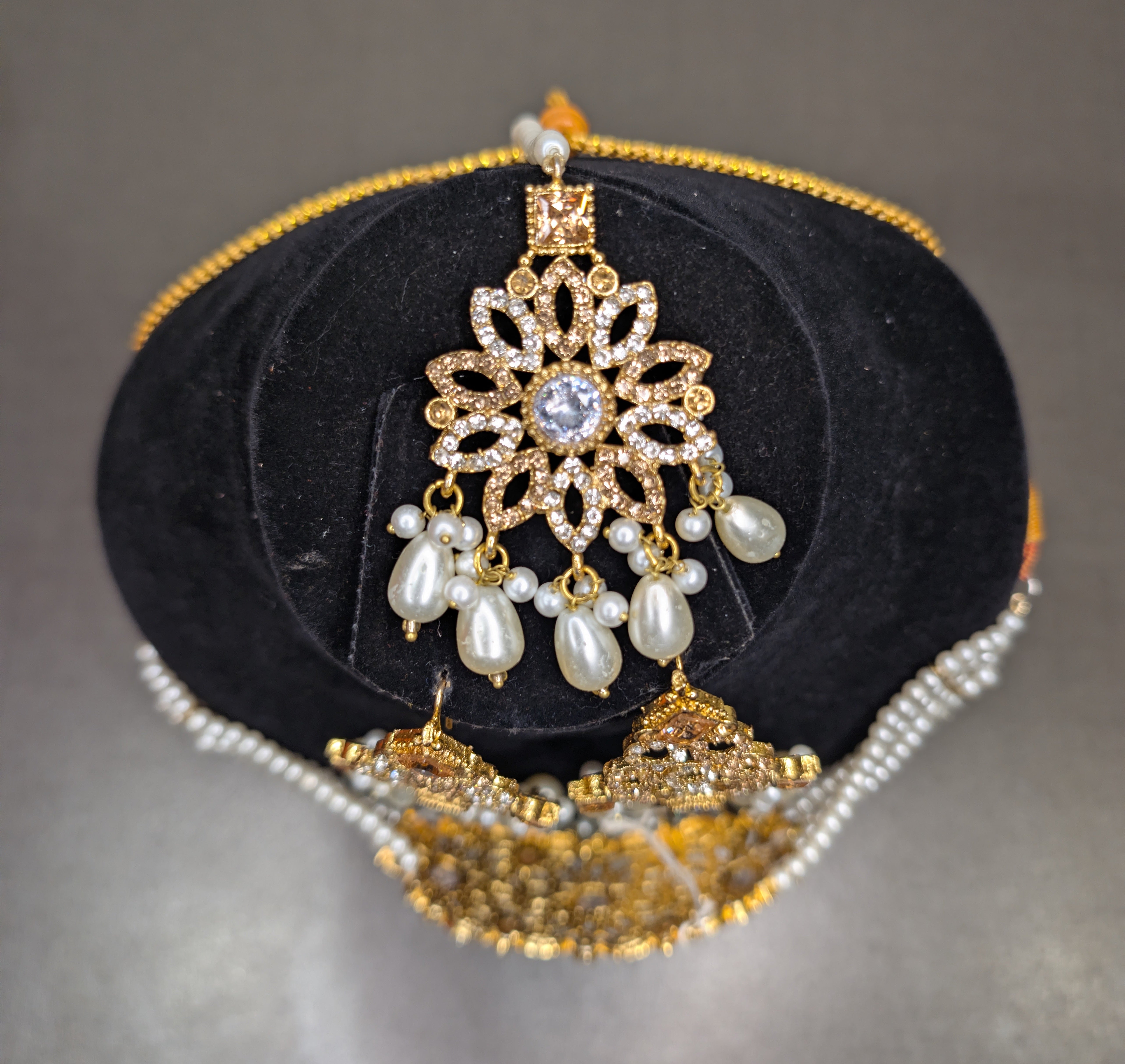 Decorative headpiece with pearls and gold details on a black cushion