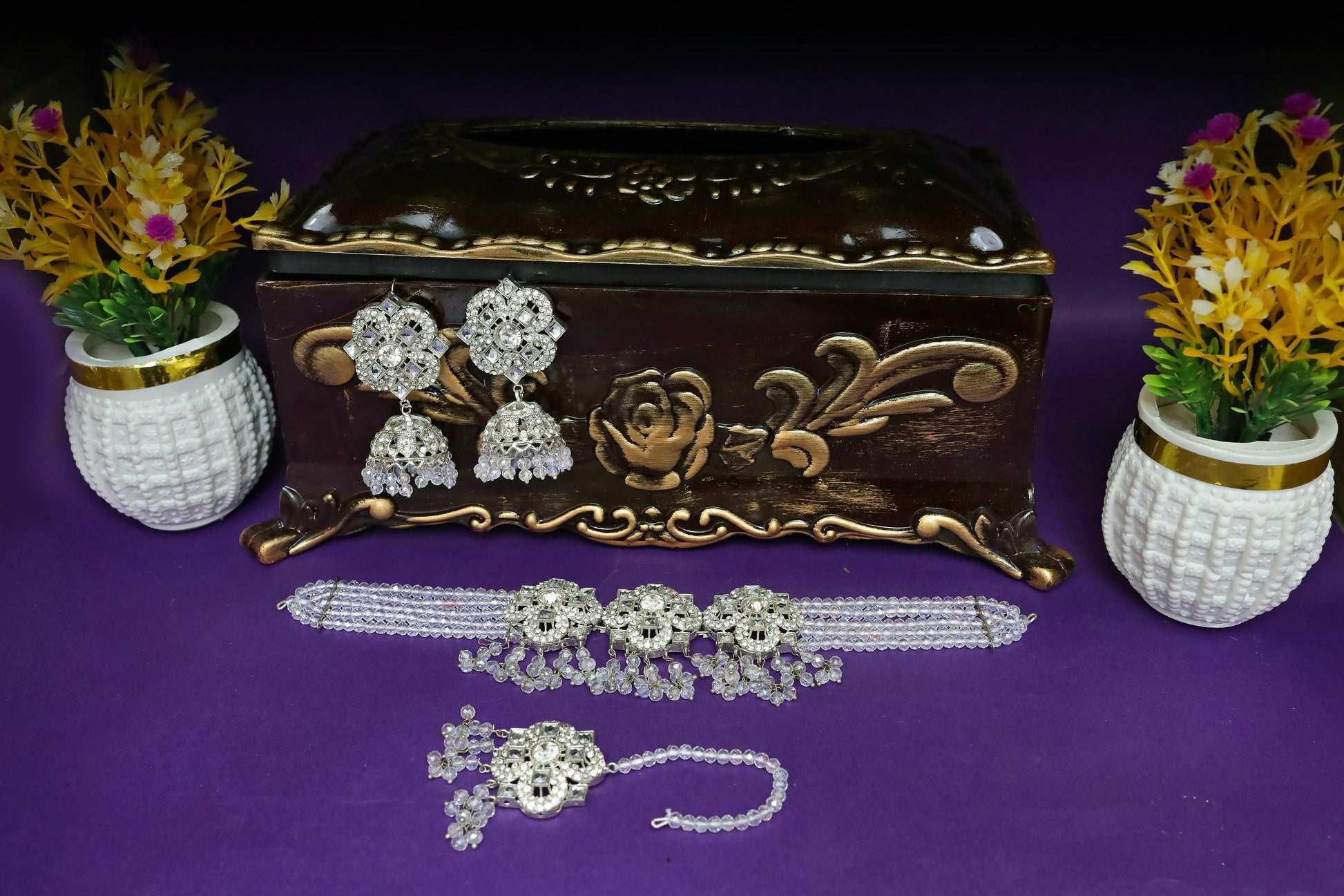 Decorative jewelry box with earrings, necklace, and bracelet on a purple surface with floral decorations.