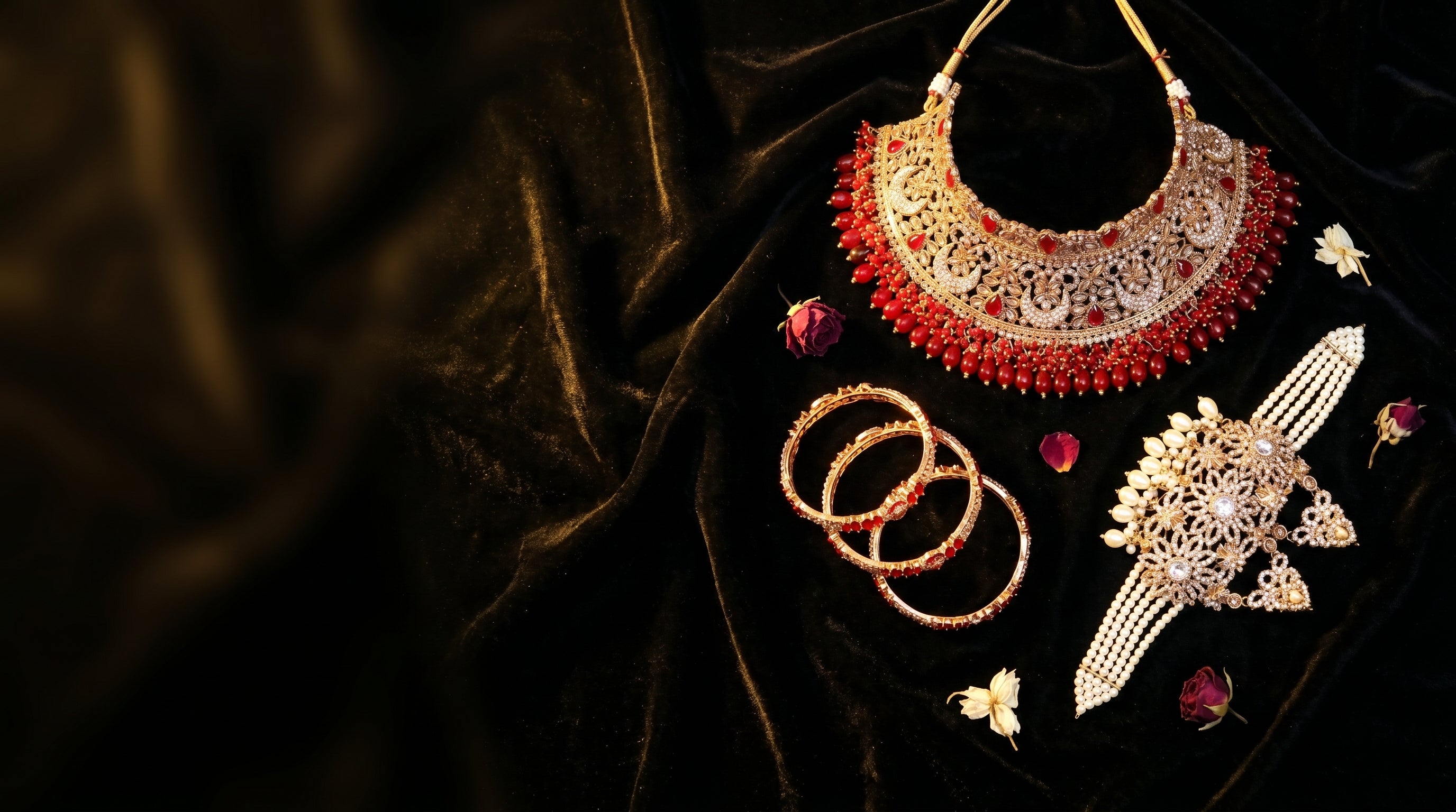 Decorative jewelry set including a necklace, bangles, and a decorative item on a dark fabric background Hero Banner