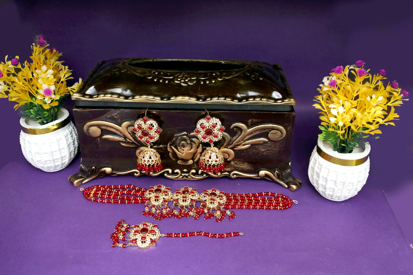 Decorative jewelry set with earrings, necklace, and bracelet on a purple background with floral arrangements.