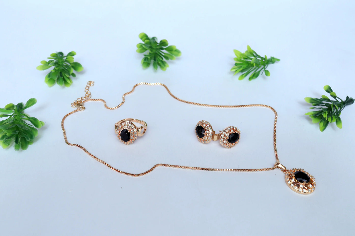 Gold Pendent with black accents on a light blue background with green plants.