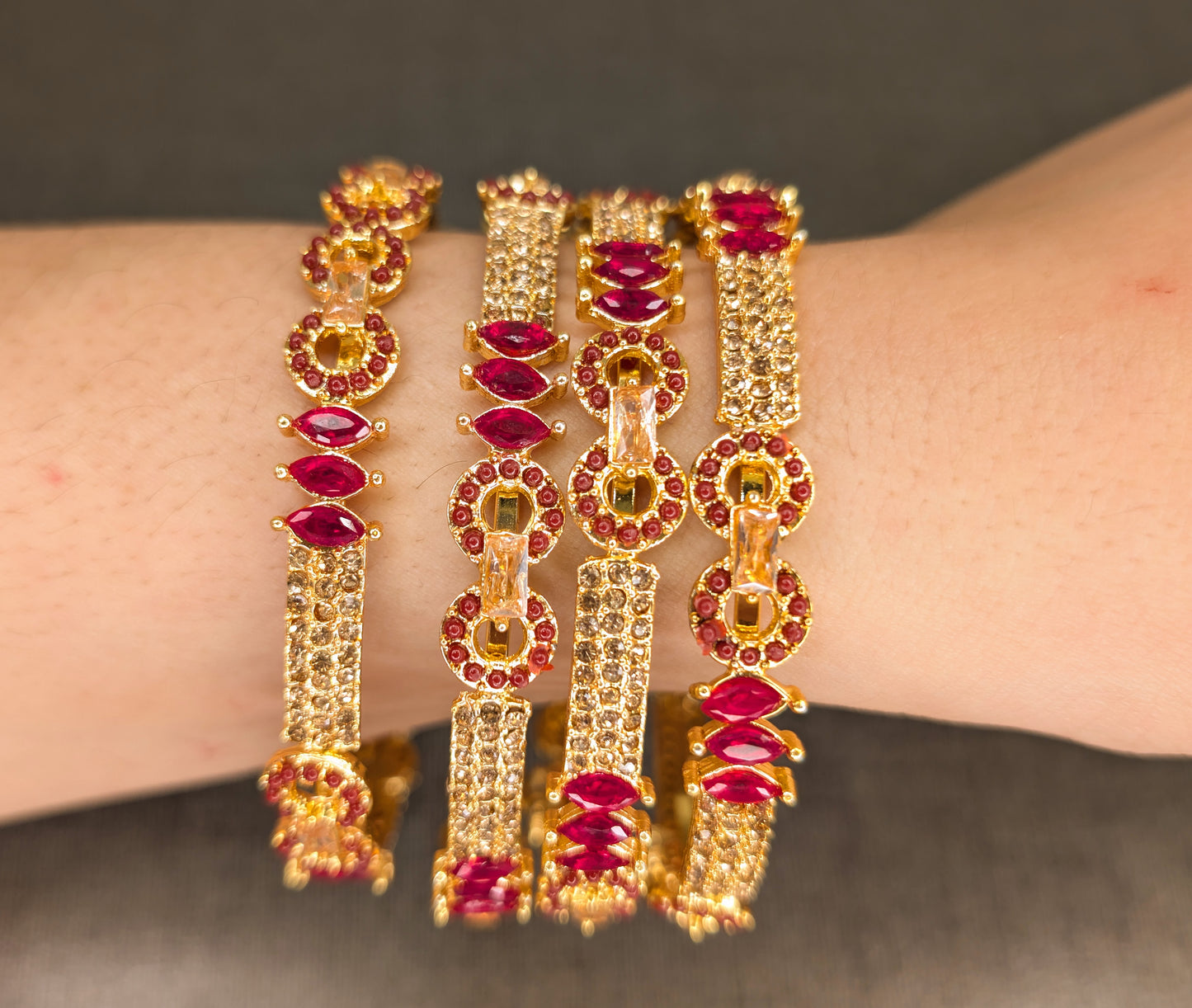 Gold and red gemstone bangles on a wrist against a dark background