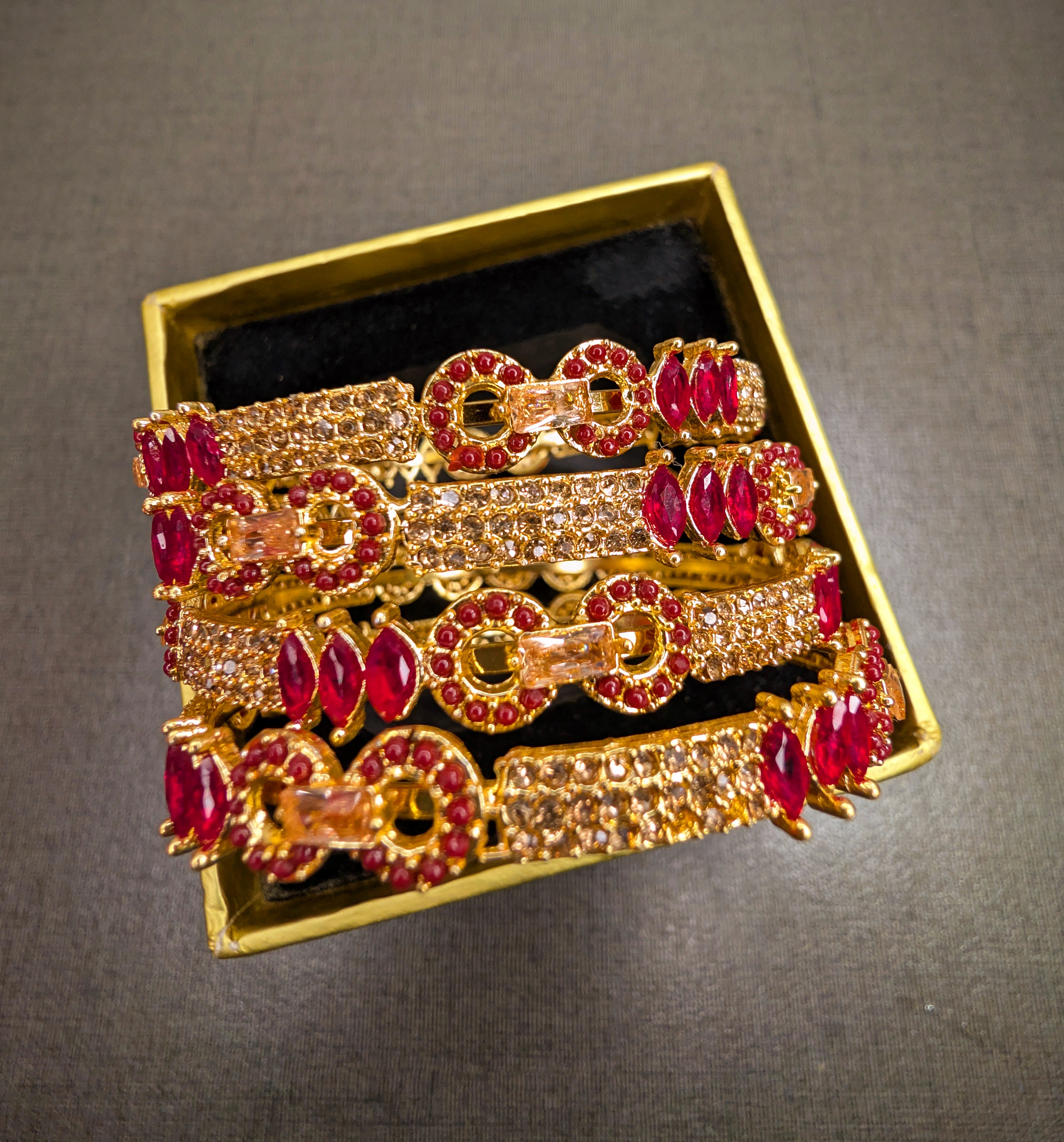 Gold and red gemstone bracelet set in a gold box on a gray background