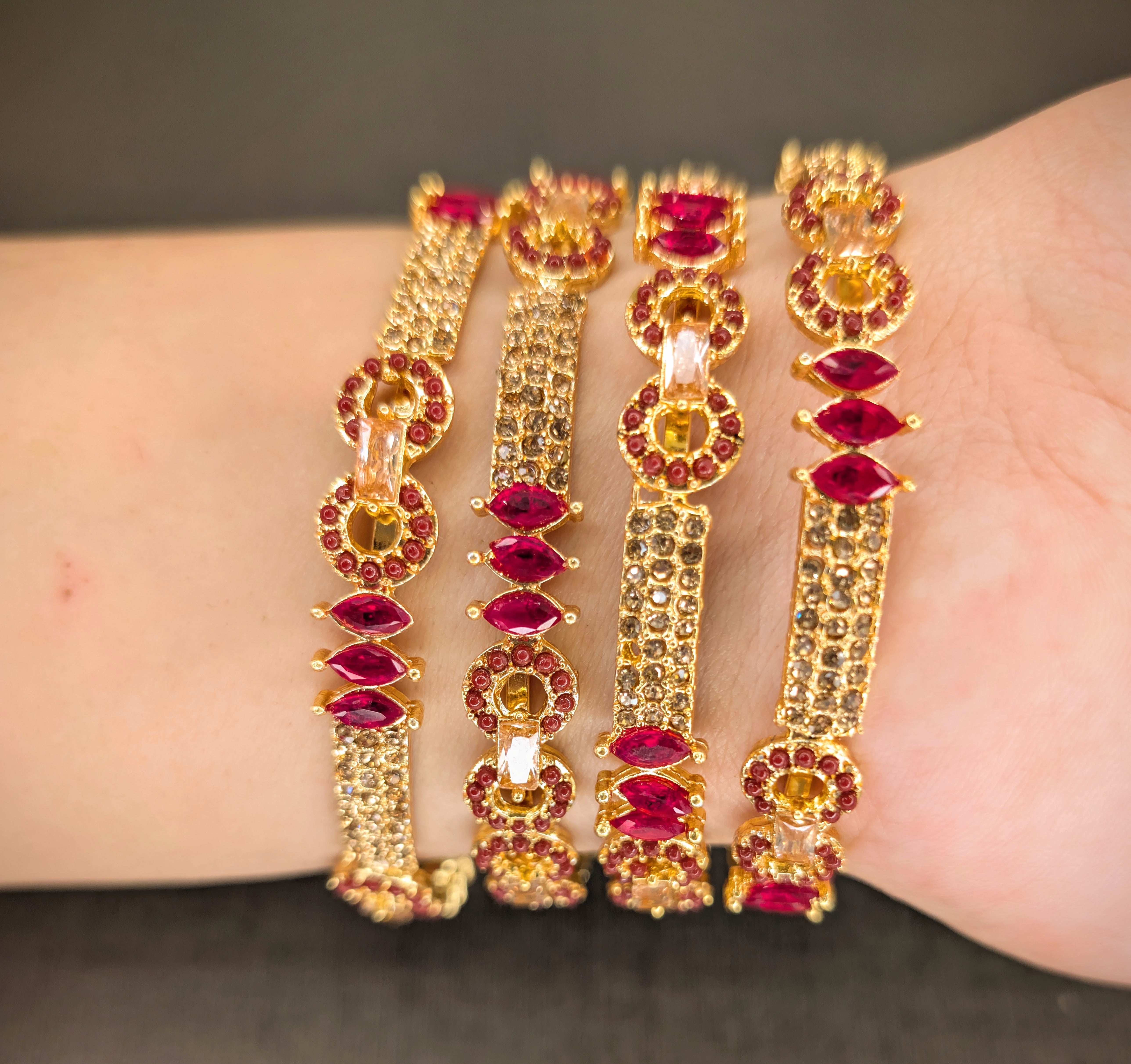 Gold and red gemstone bracelets on a wrist against a neutral background