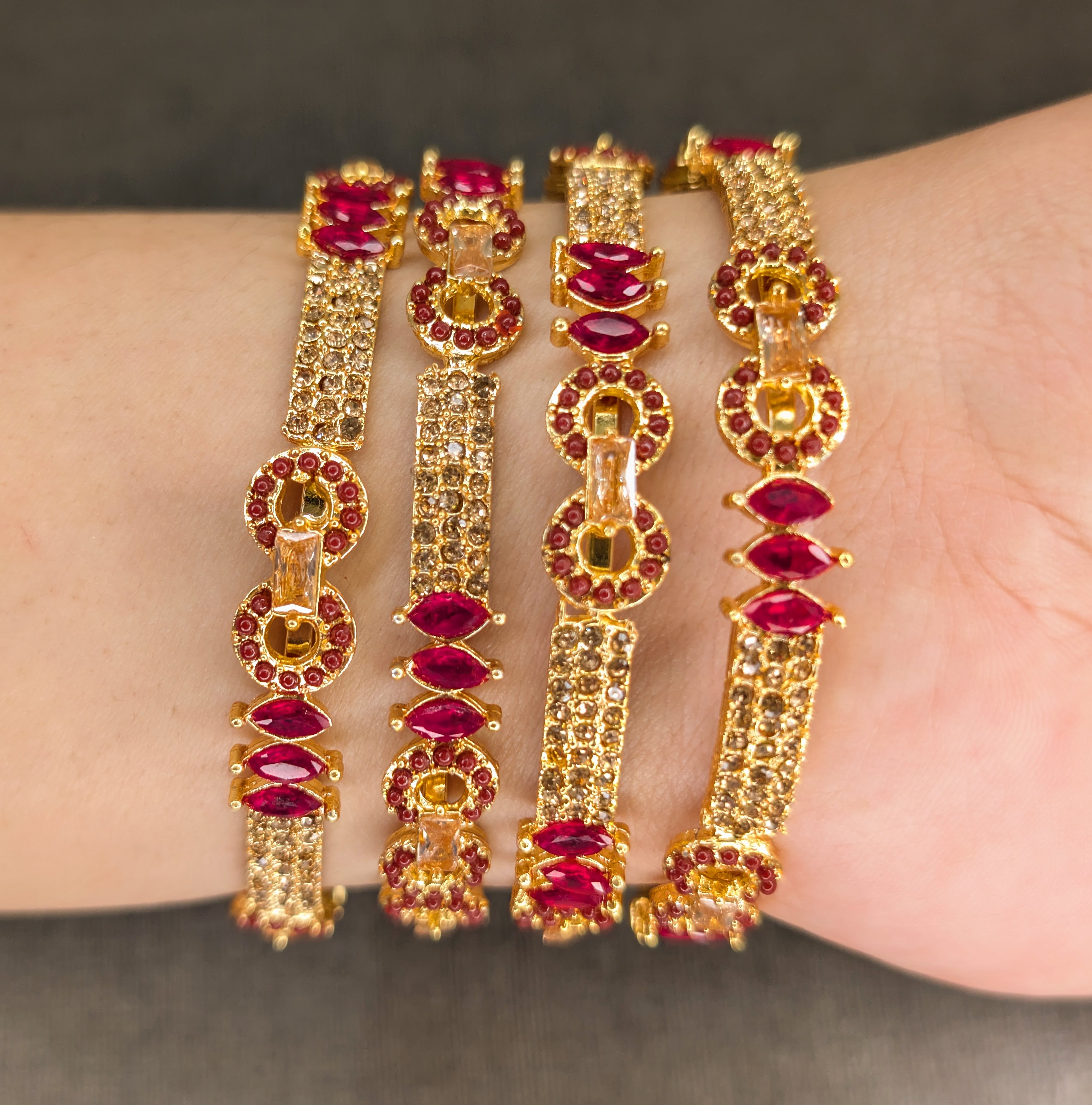 Gold and red gemstone bracelets on a wrist against a neutral background