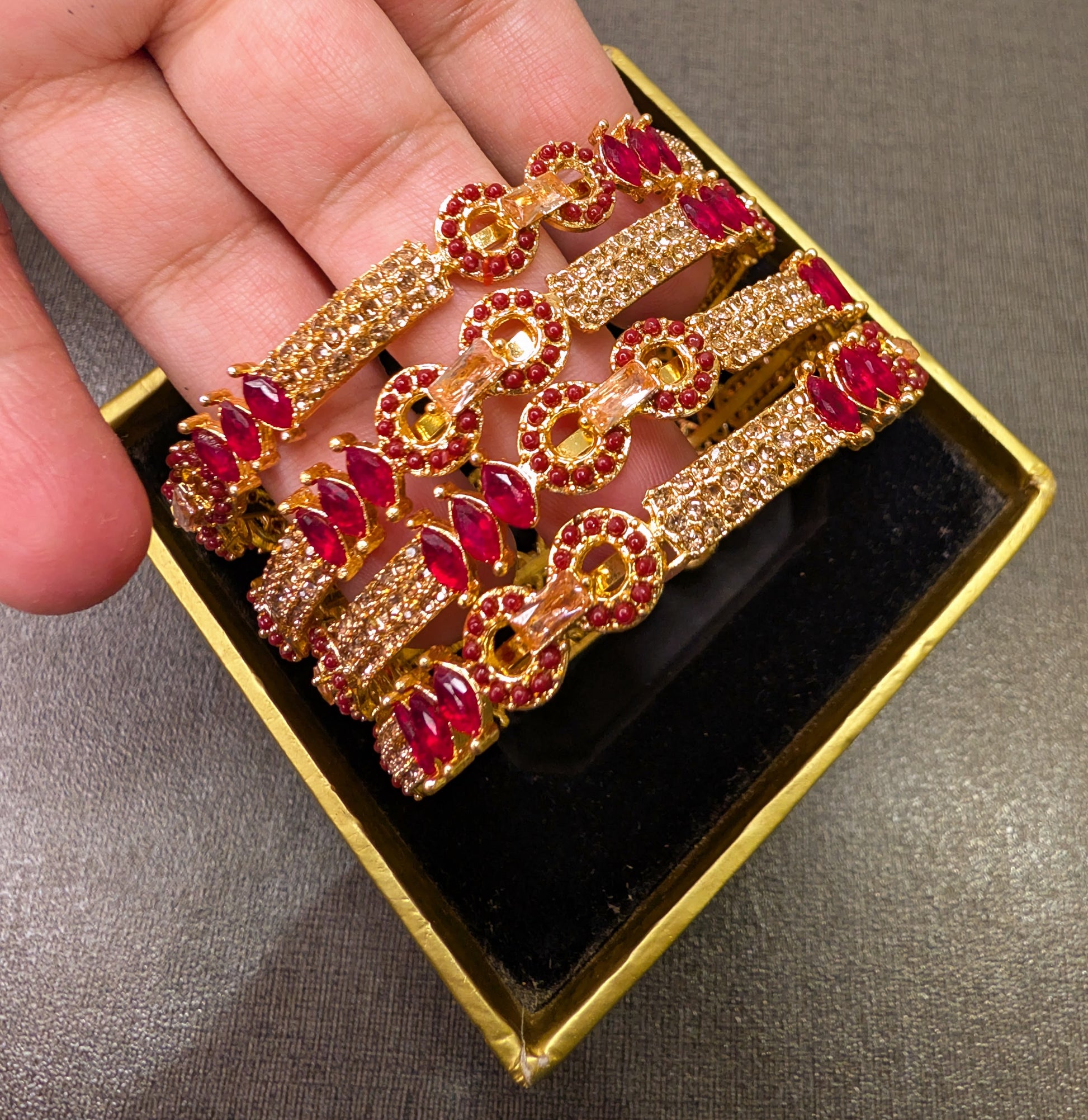 Gold and red gemstone brooch held by a hand on a gray surface