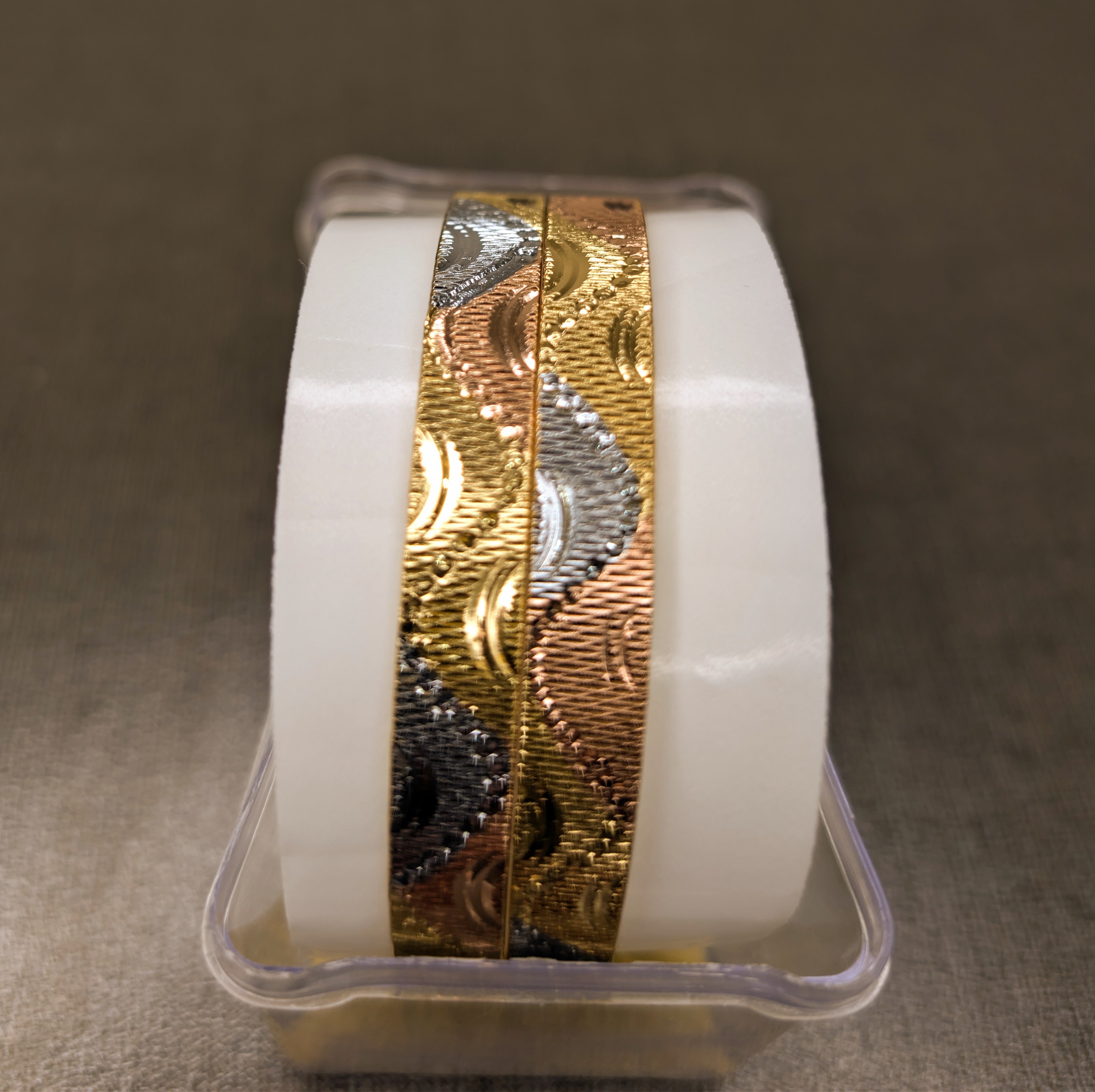 Gold and silver ribbon roll in a clear container on a textured surface