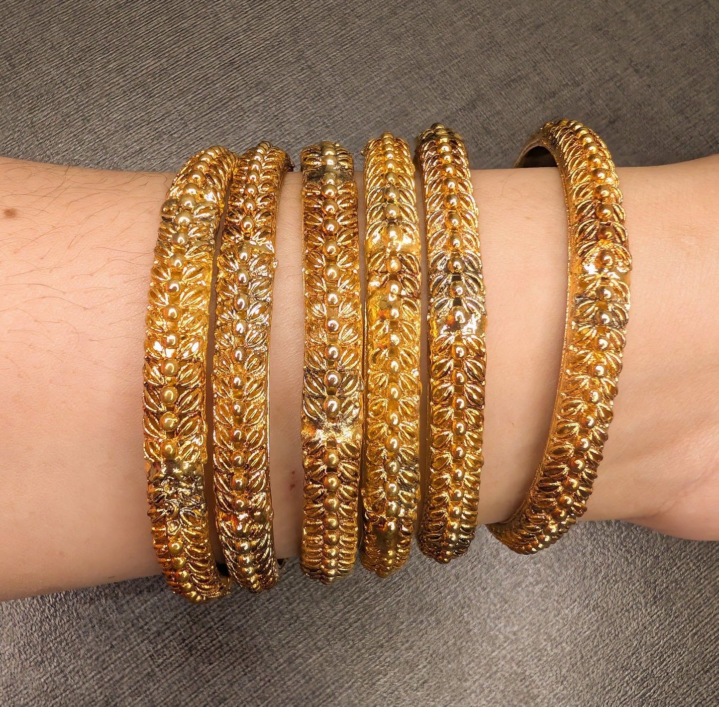 Gold bangles on a person's wrist against a gray background