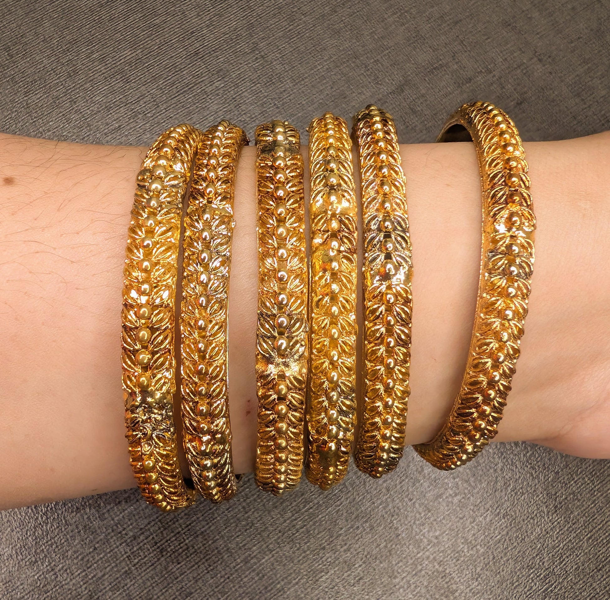 Gold bangles on a person's wrist against a gray background