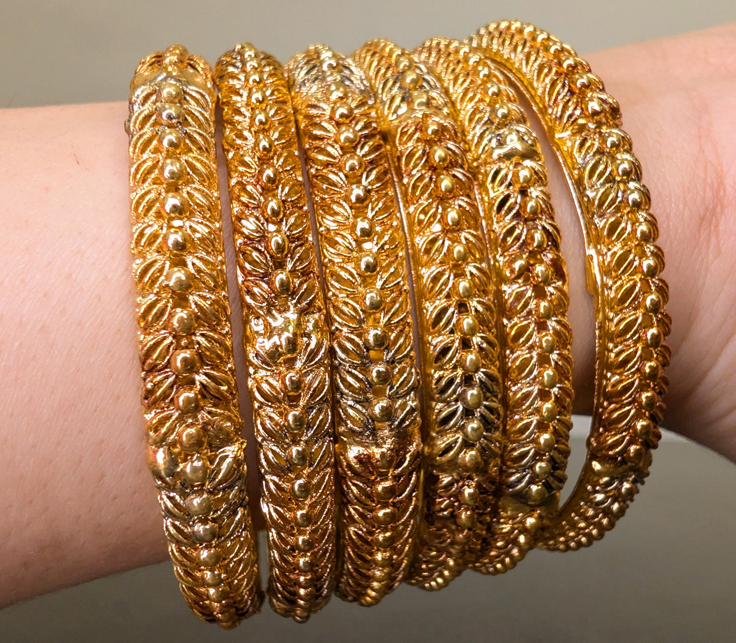 Gold bangles on a wrist against a neutral background