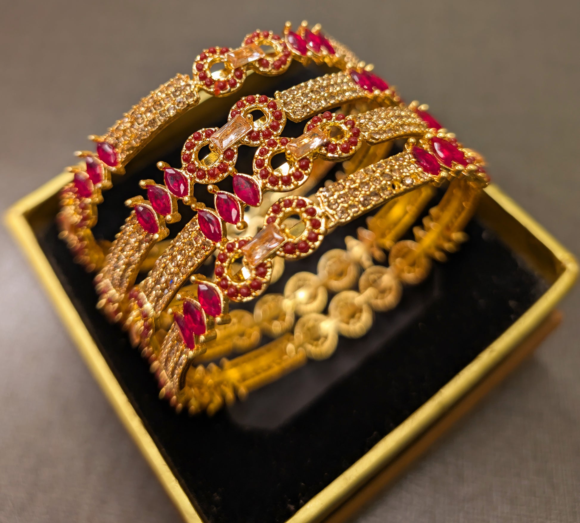 Gold bangles with red stones on a black box