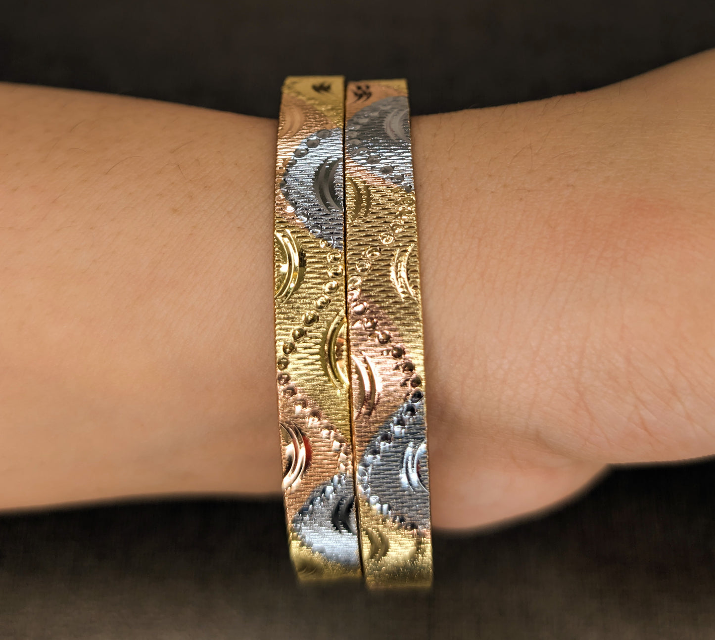 Gold bracelet with intricate design on a wrist against a dark background