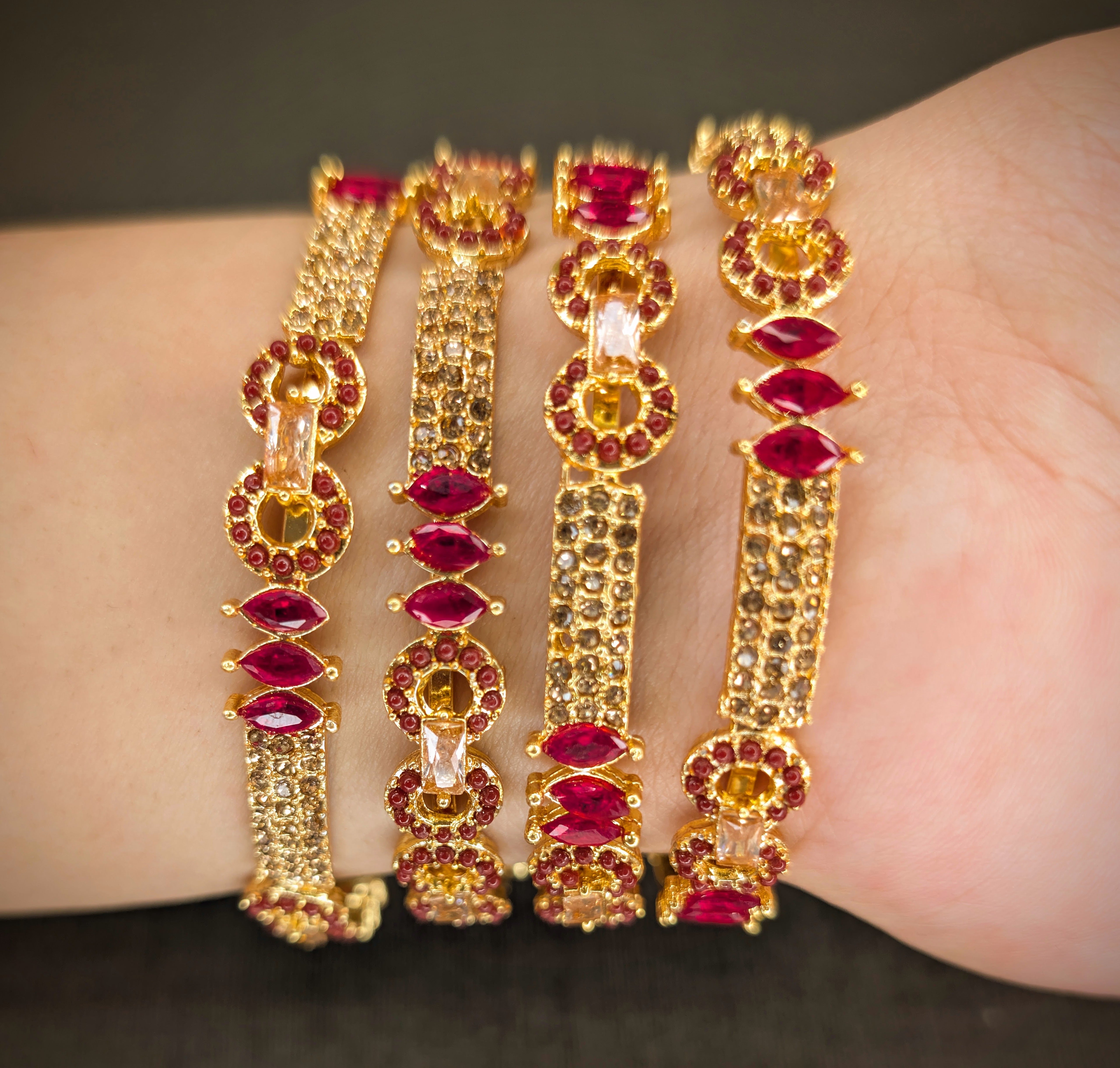 Gold bracelets with red gemstones on a wrist against a dark background