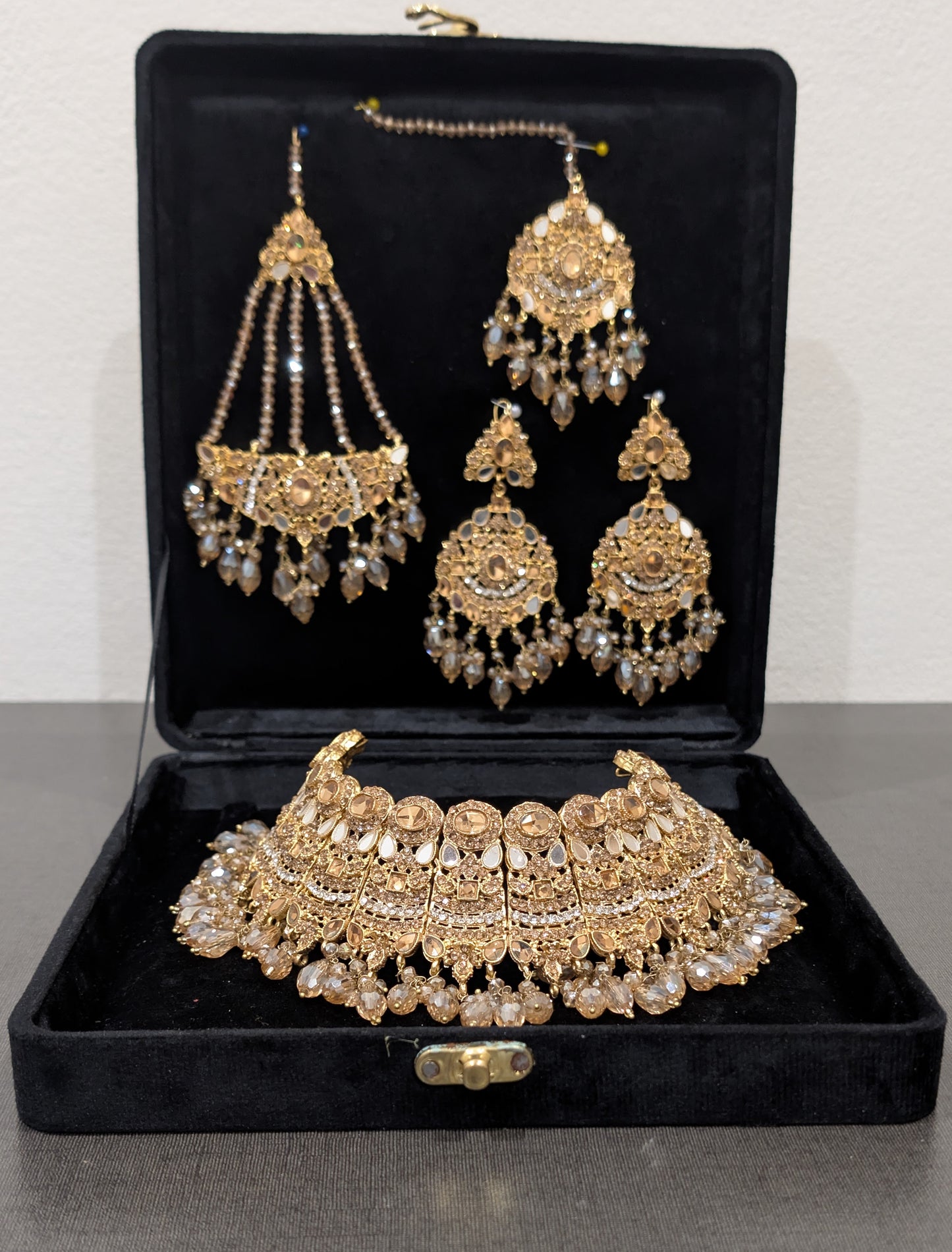 Gold jewelry set with necklace, earrings, and choker in a black box on a gray surface.
