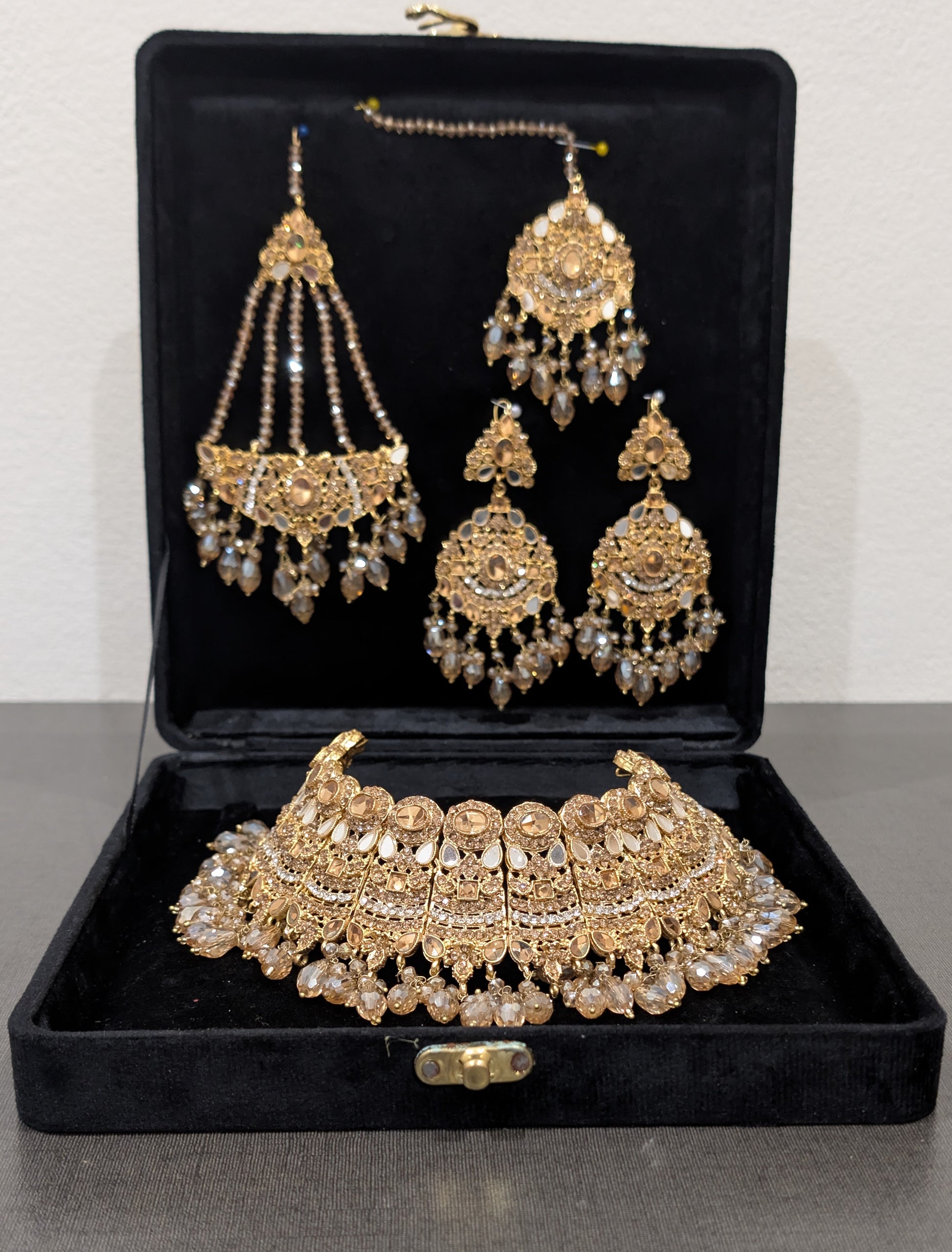 Gold jewelry set with necklace, earrings, and choker in a black box on a gray surface.