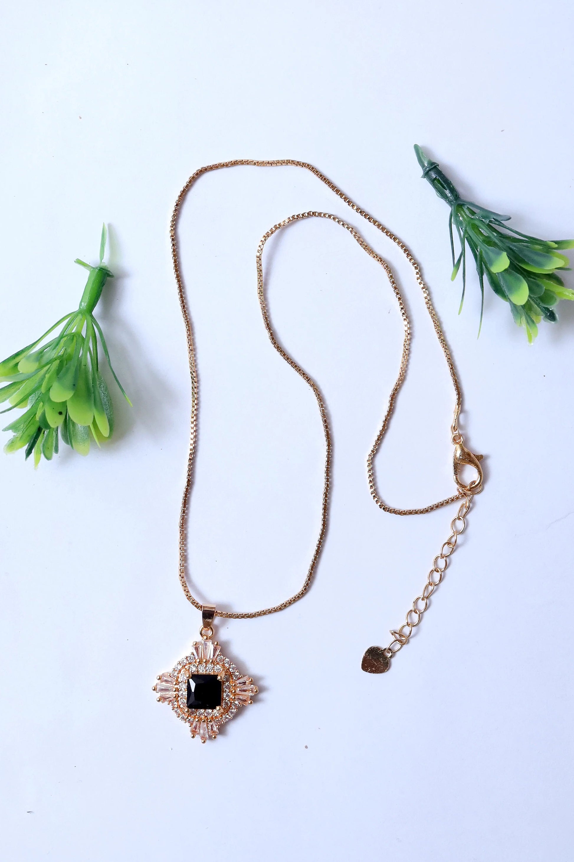 Gold necklace with a decorative pendant on a light blue background with green leaves.