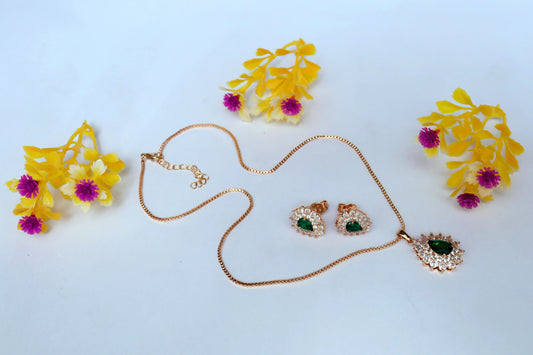 Gold necklace with heart pendant and matching earrings on a light blue background with yellow and pink flowers.
