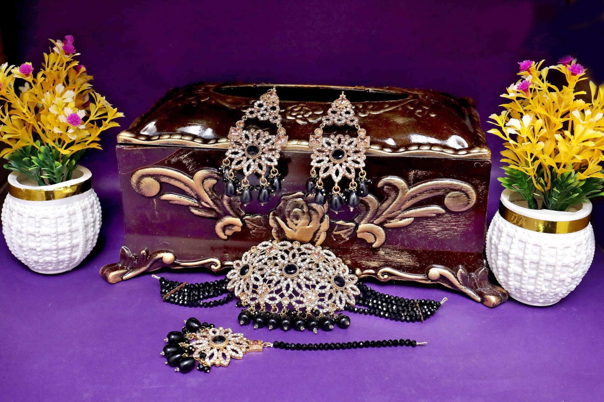 Jewelry set with earrings, necklace, and bangles on a decorative box with flowers on a purple background
