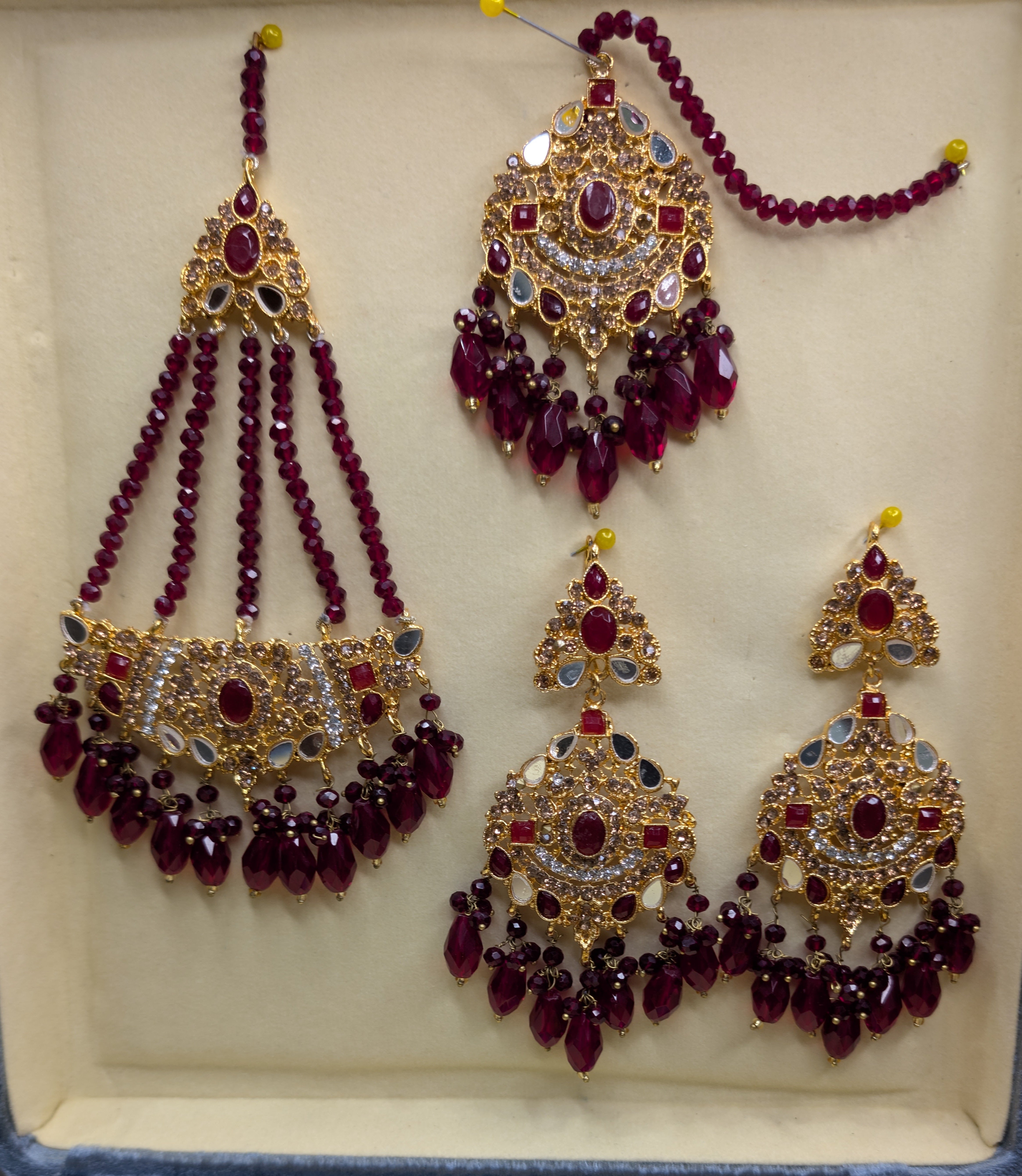 Jewelry set with maroon beads and gold accents on a beige background