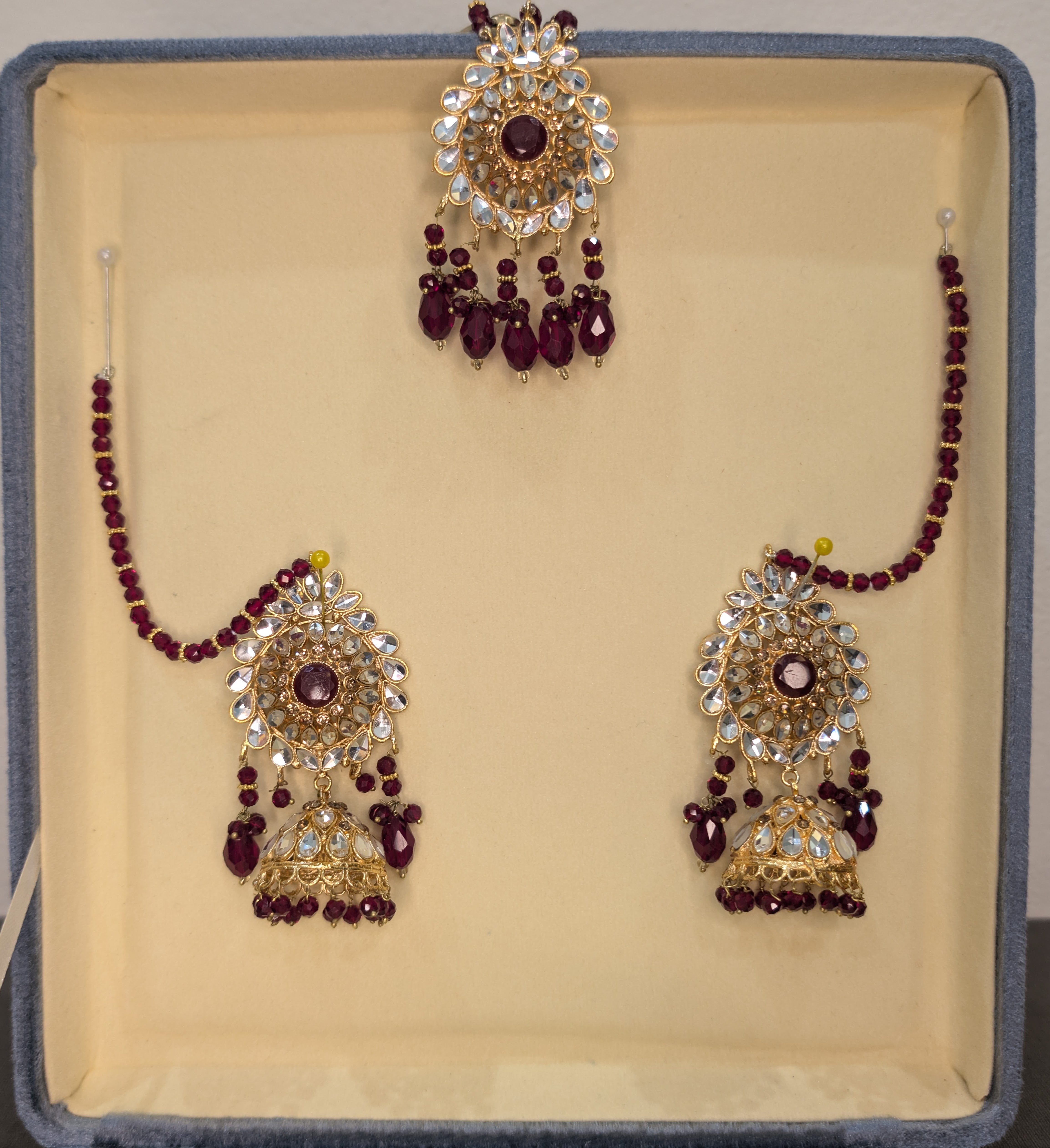 Jewelry set with maroon beads and gold accents on a beige cushioned box.