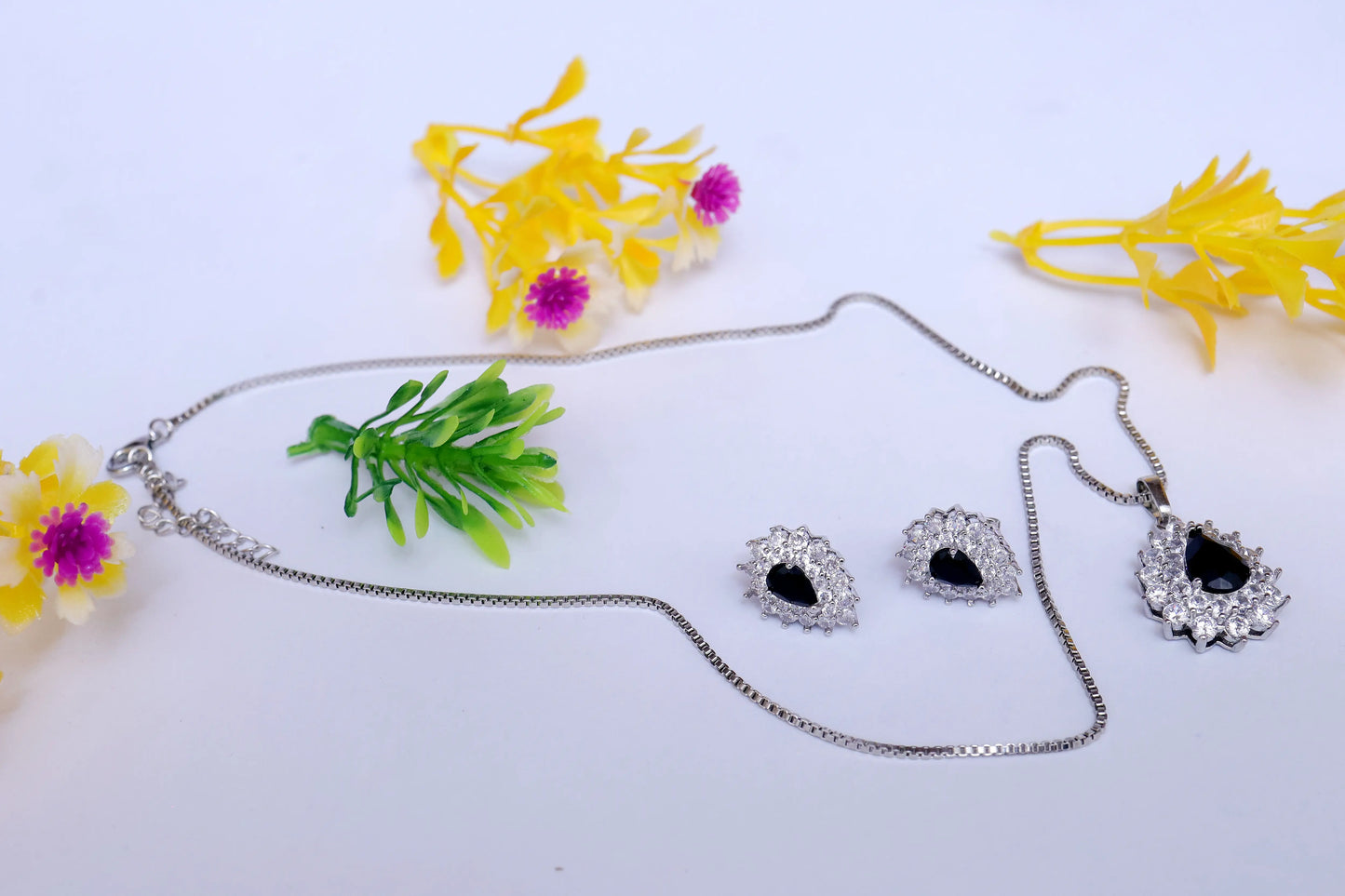 Jewelry set with necklace and earrings on a white background with artificial flowers.