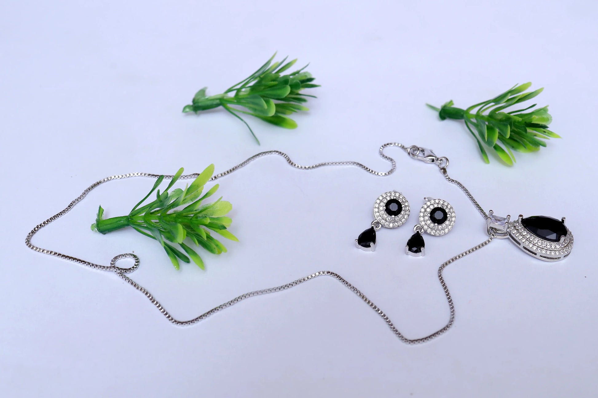 Jewelry set with necklace and earrings on a white background with green plants.