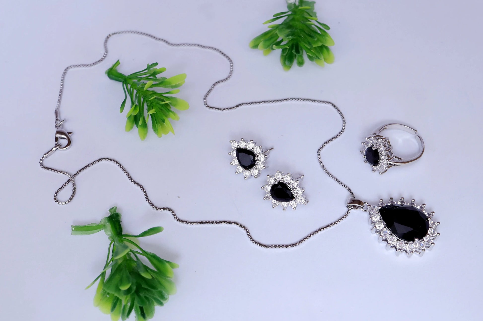 Jewelry set with necklace, earrings, and ring on a light gray background with green leaves.
