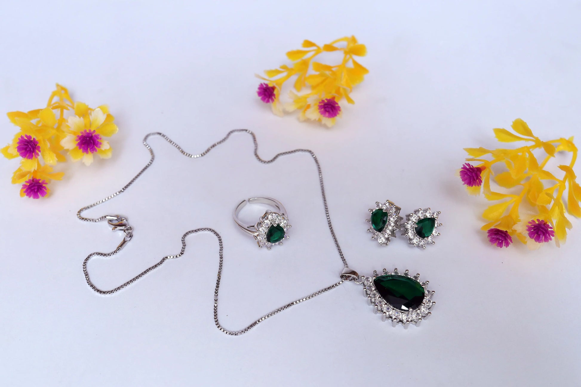 Jewelry set with necklace, ring, and earrings on a white background with yellow flowers.
