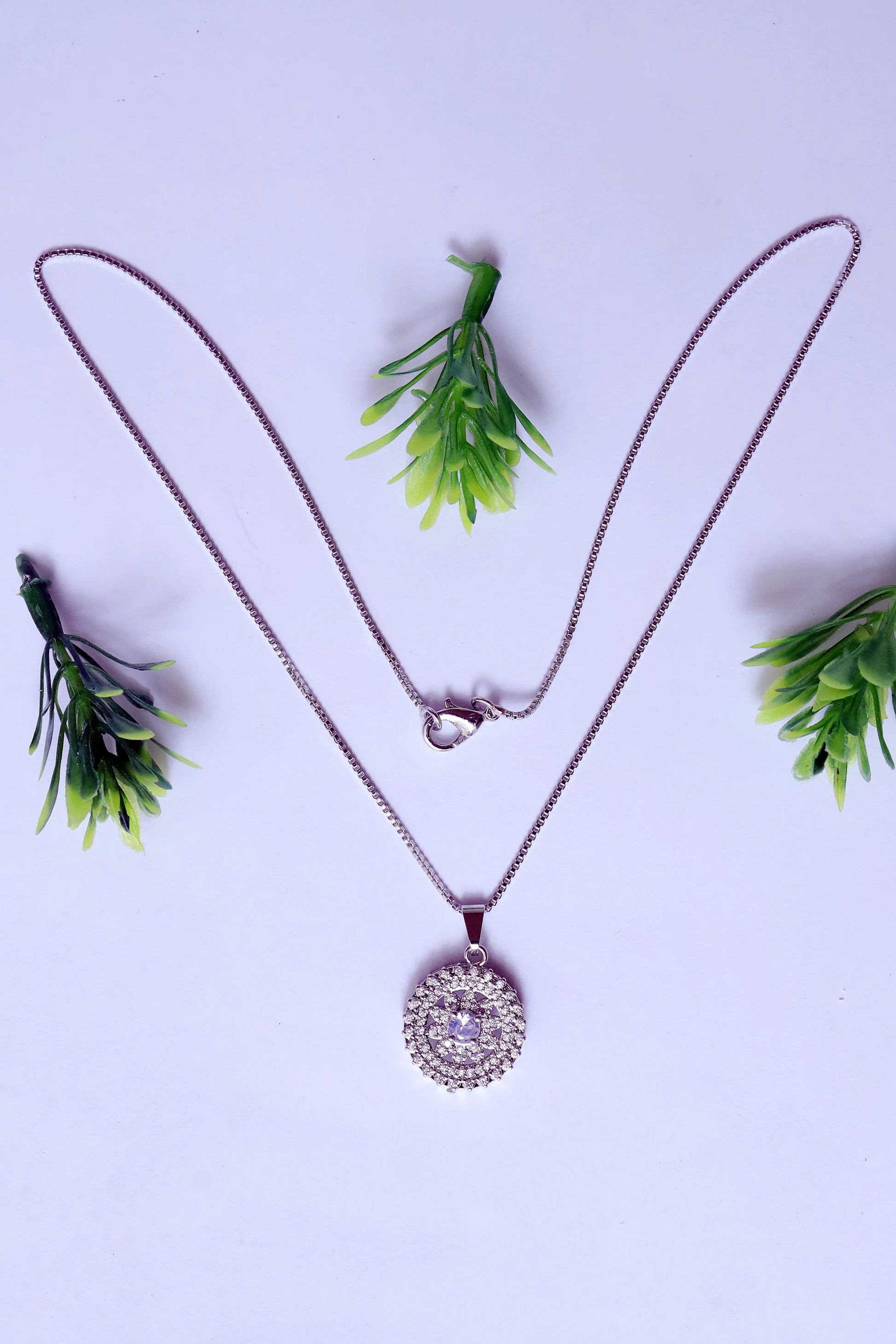 Necklace with a circular pendant on a light purple background with green leaves.