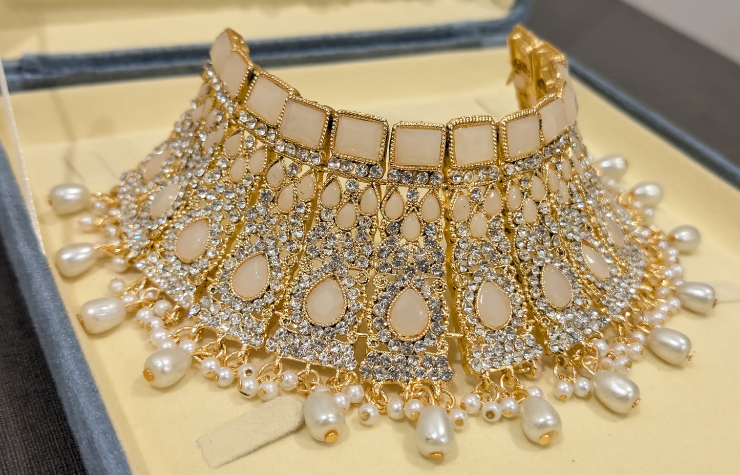 Ornate choker necklace with gold accents and pearls on a textured surface picture captured from tilted angle