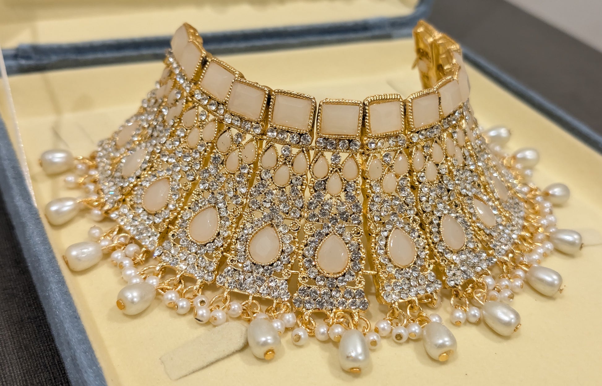 Ornate choker necklace with gold accents and pearls on a textured surface picture captured from tilted angle