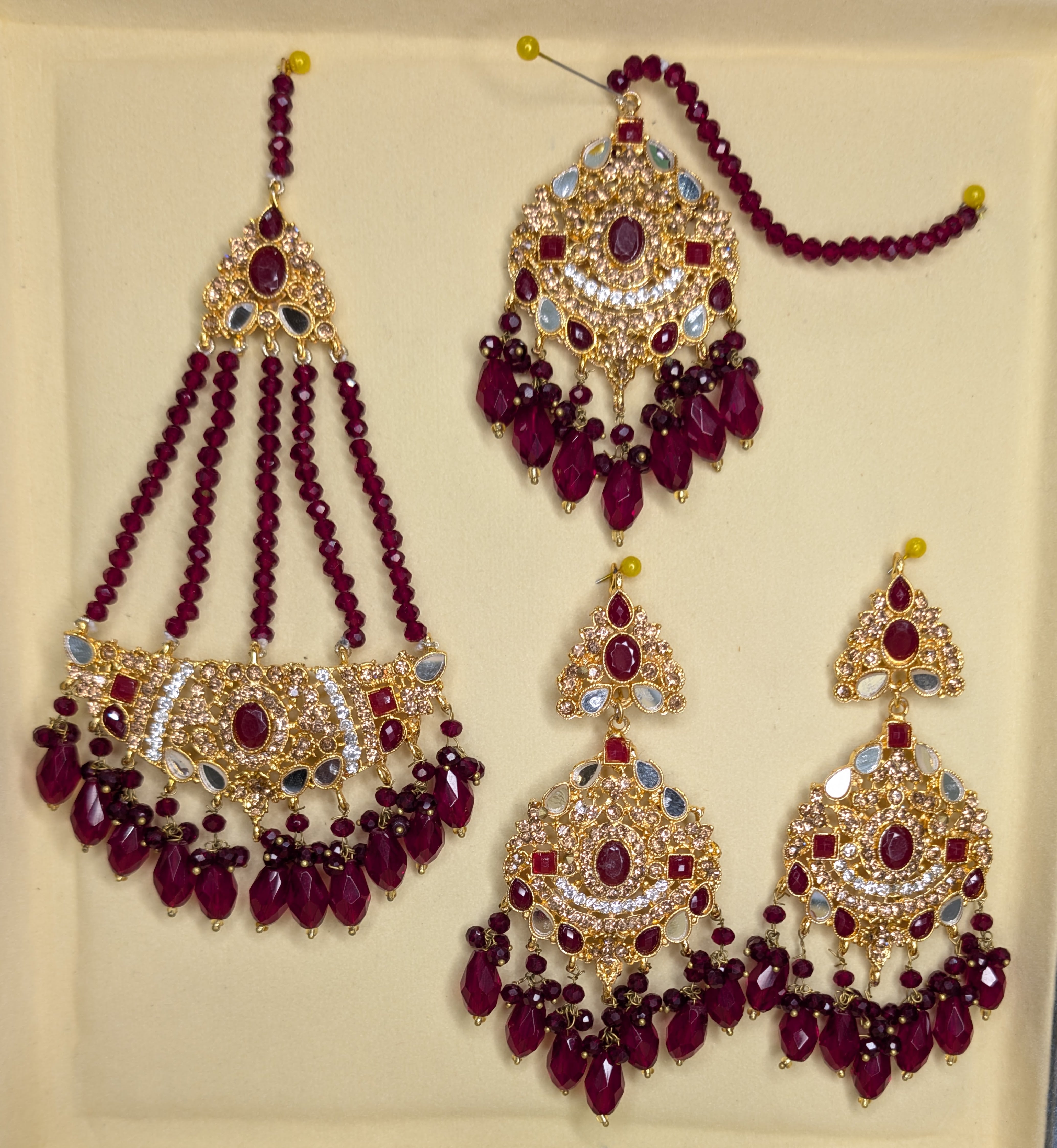 Ornate earrings with red beads and gold accents on a beige background