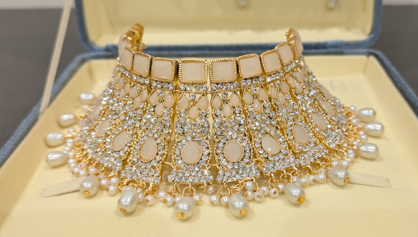 Ornate gold and pearl necklace on a beige cushion with a jewelry box in the background.