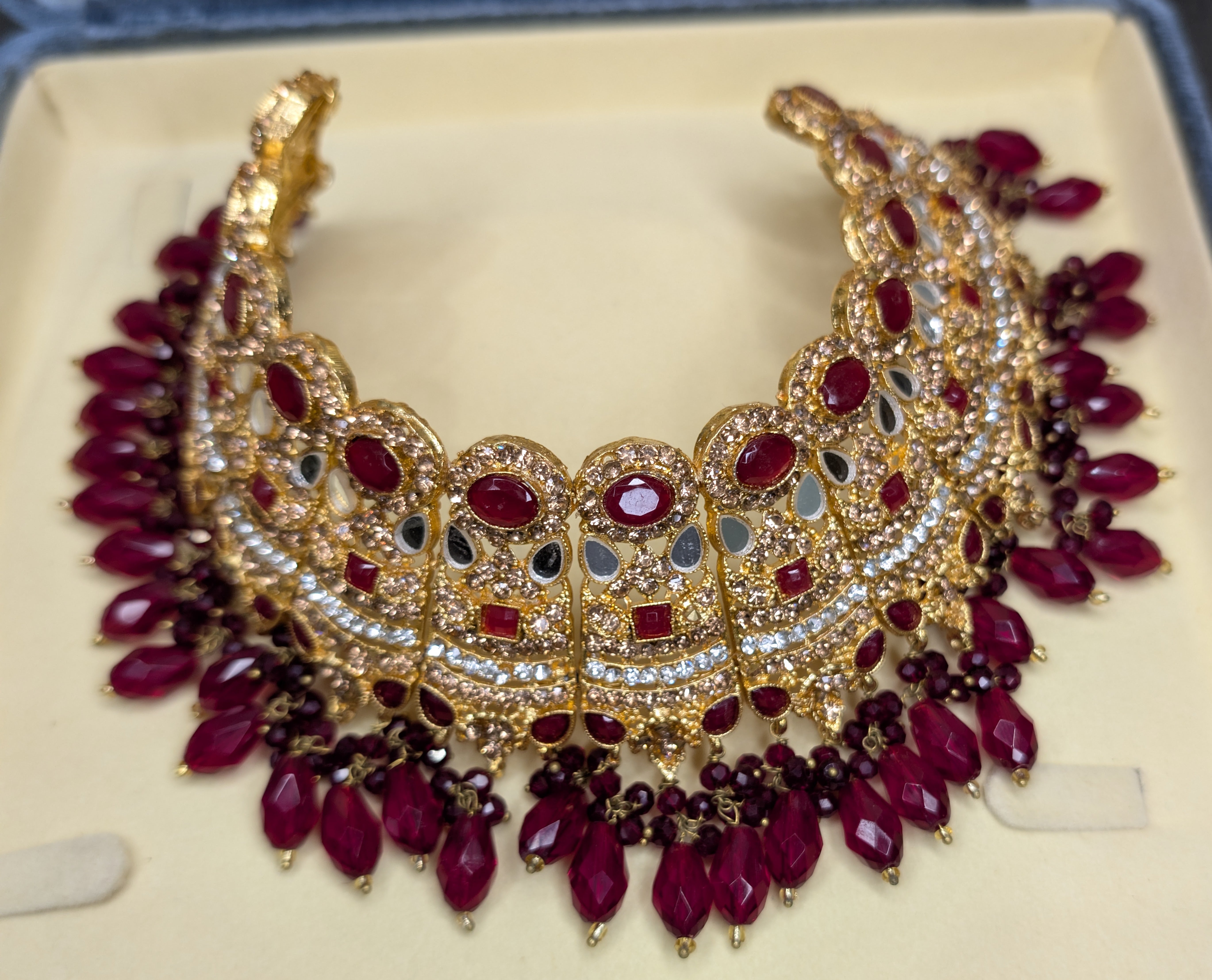 Ornate gold and red necklace on a beige cushion
