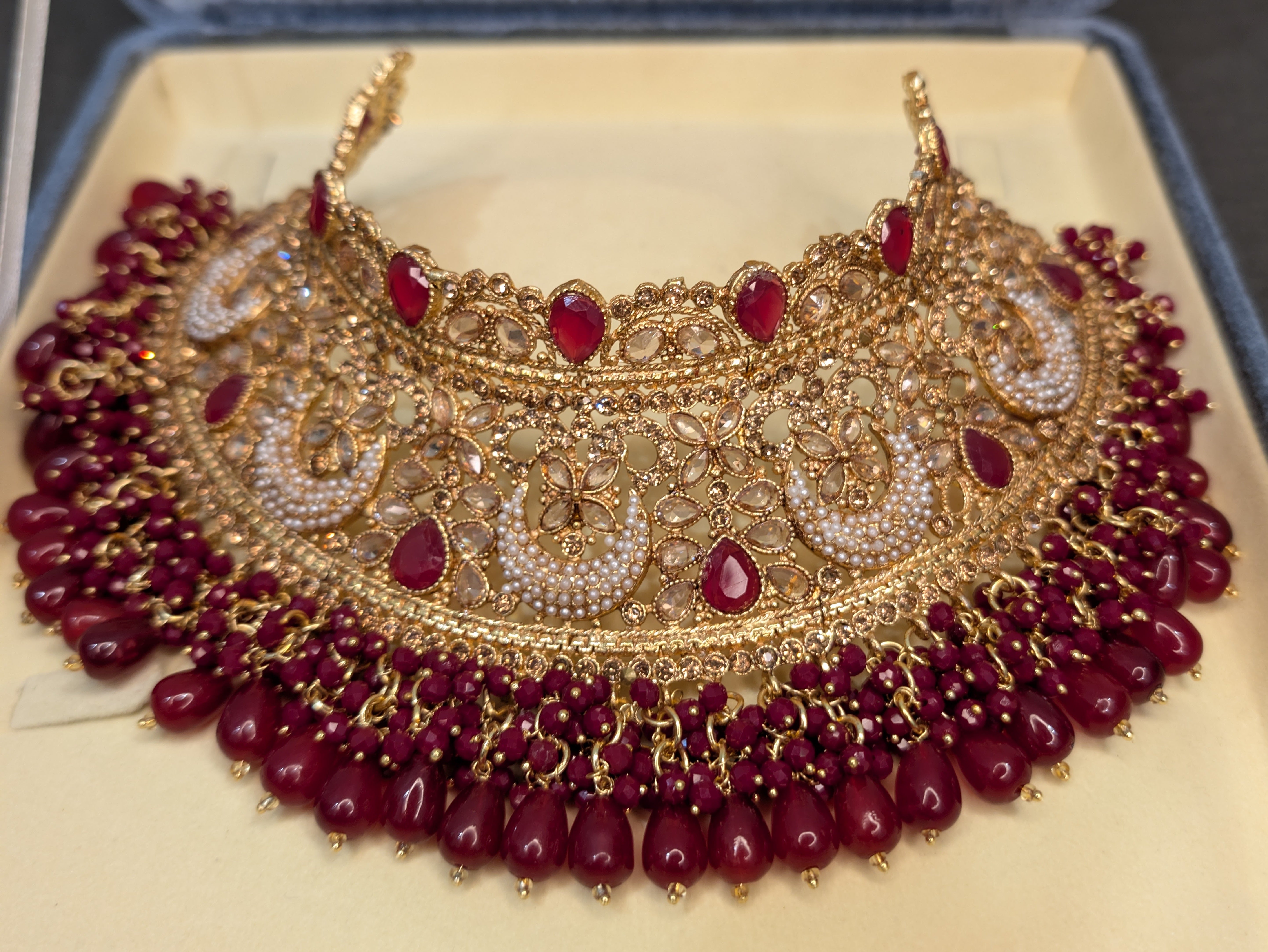 Ornate gold necklace with red beads on a beige cushion