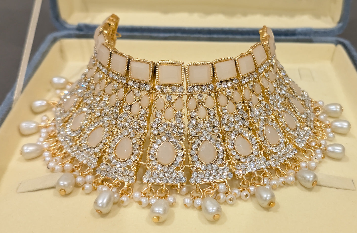 Ornate necklace with pearls and gold accents on a beige background from fron view