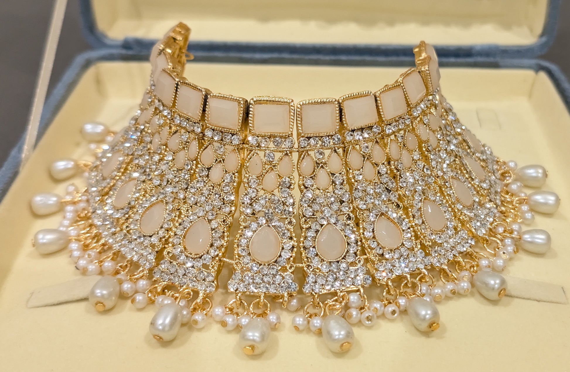 Ornate necklace with pearls and gold accents on a beige background from fron view