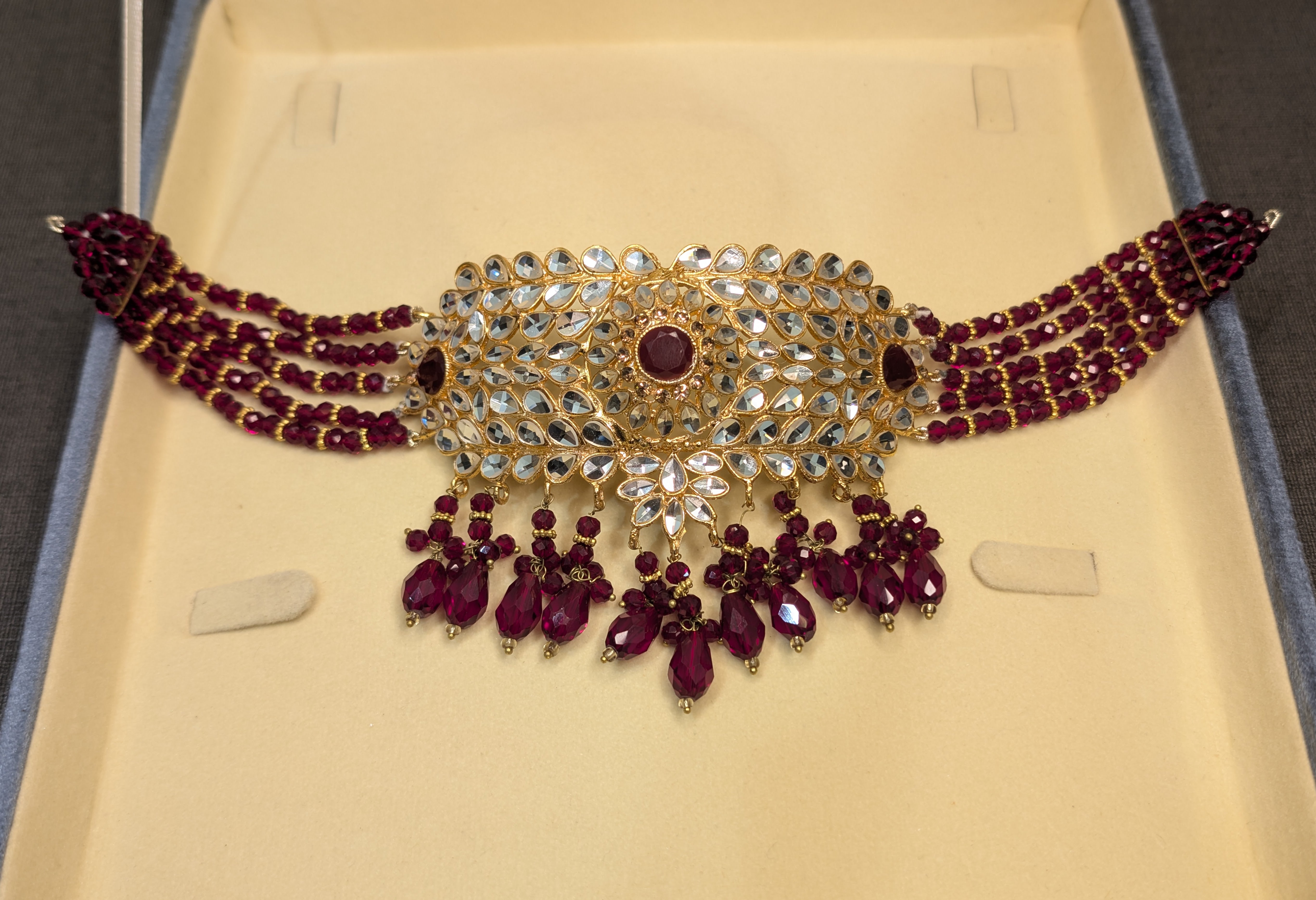 Ornate necklace with red stones and gold accents on a beige background