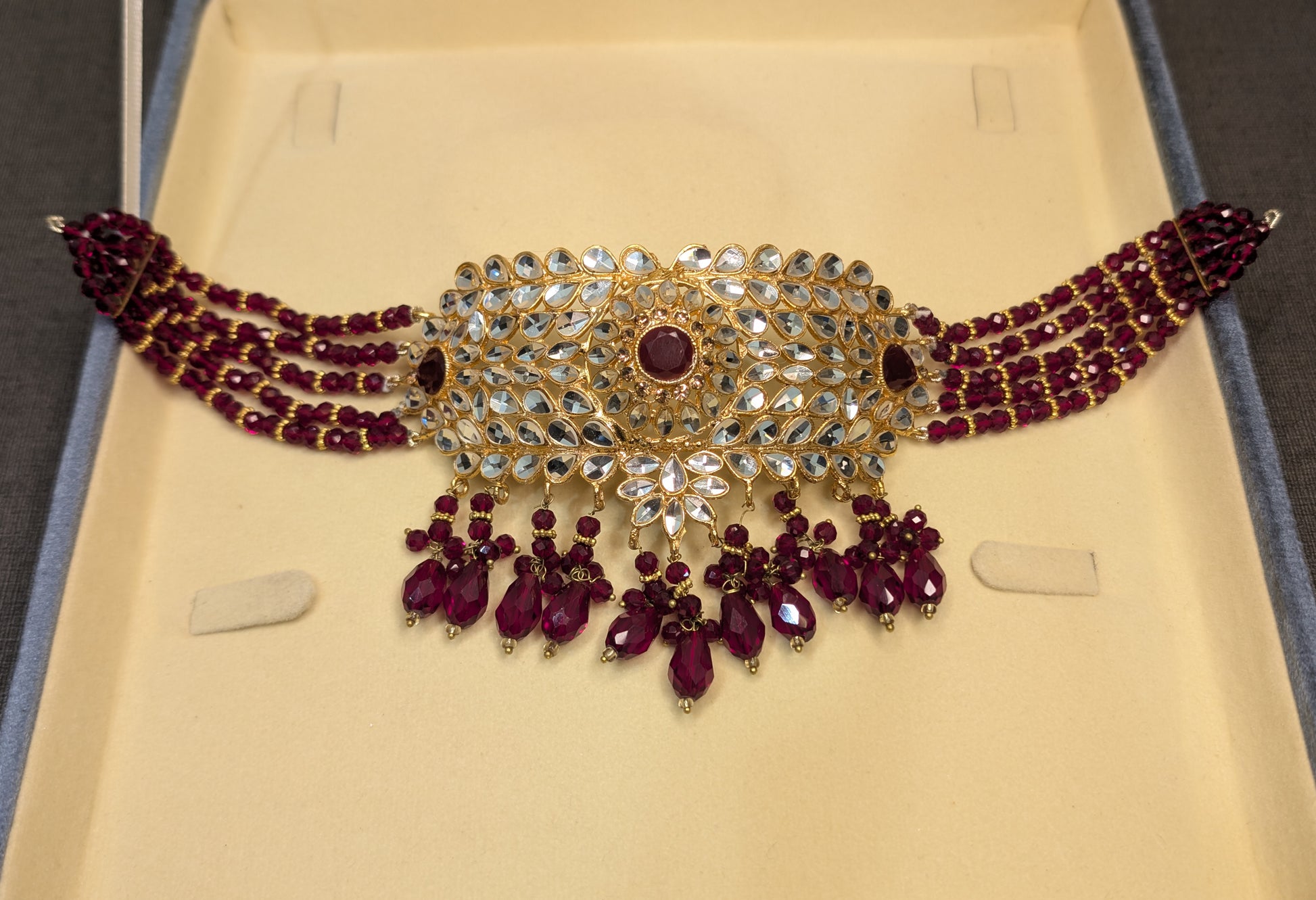 Ornate necklace with red stones and gold accents on a beige background