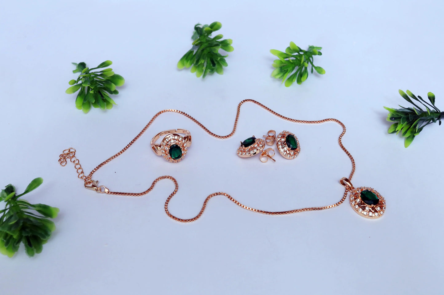 Rose gold jewelry set with green gemstones on a light blue background