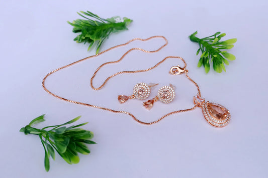 Rose gold necklace and earrings on a light gray background with green leaves.