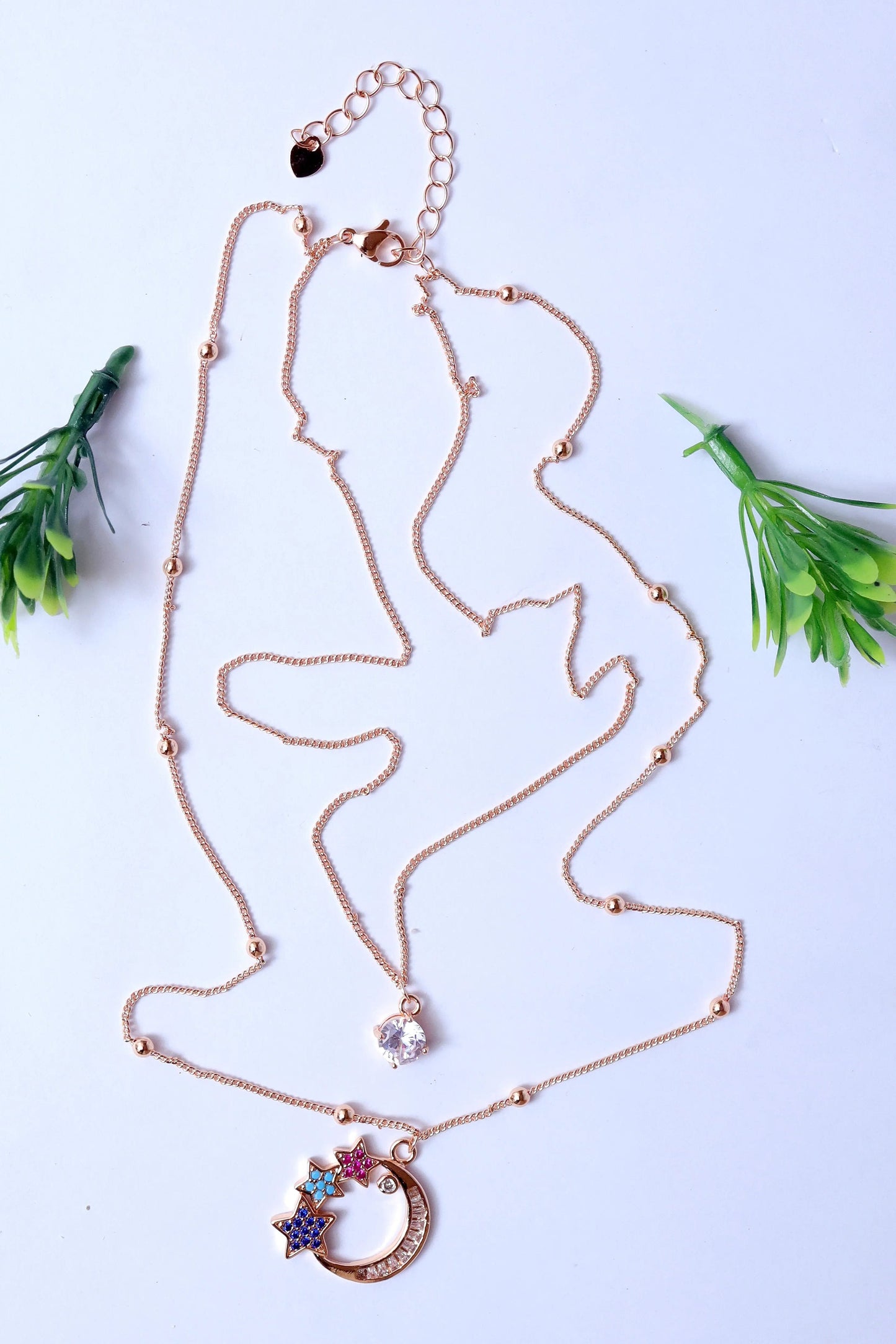 Rose gold necklace with heart and flower pendants on a light blue background