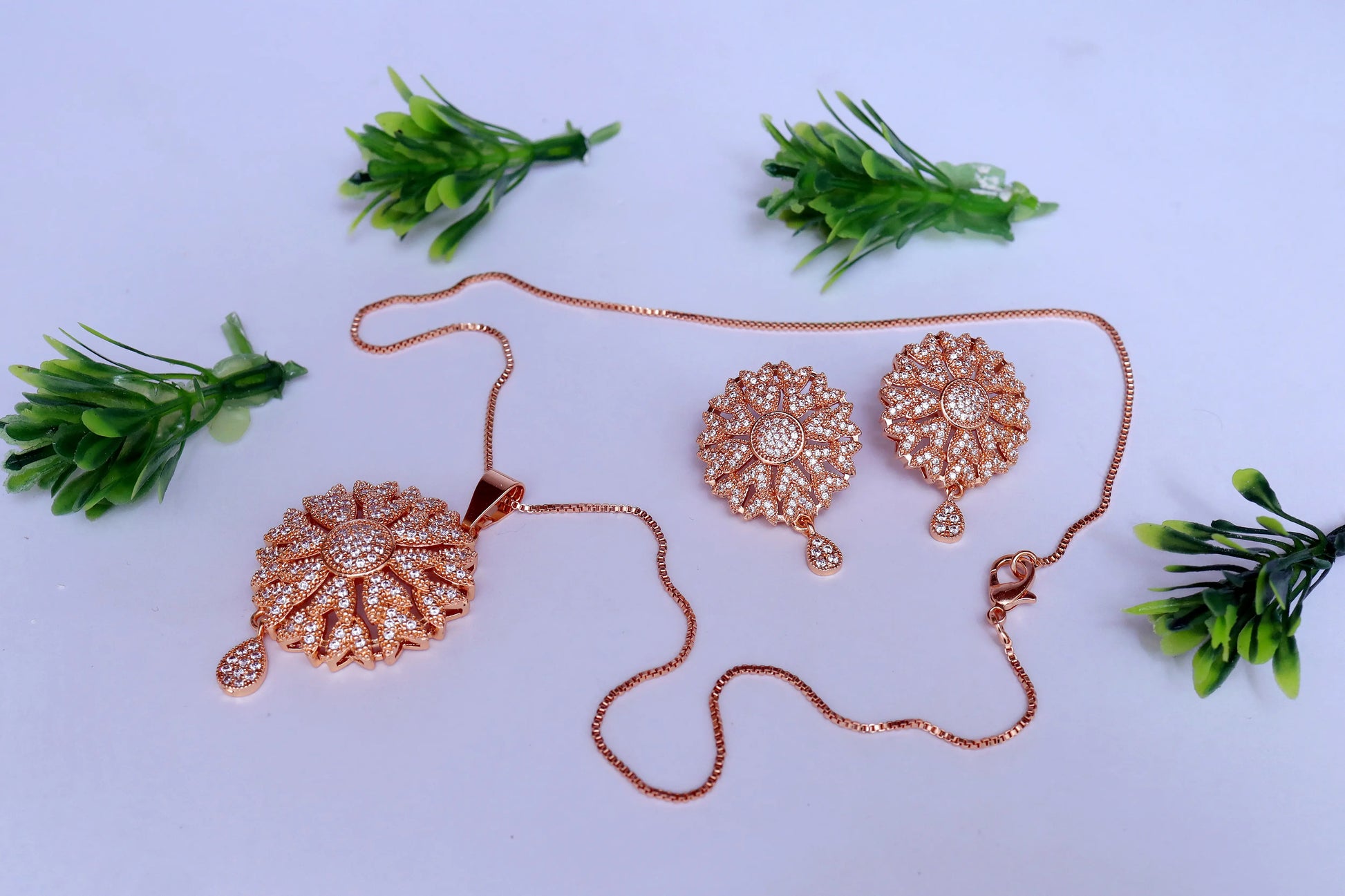 Rose gold pendent and earrings on a white background with green leaves.
