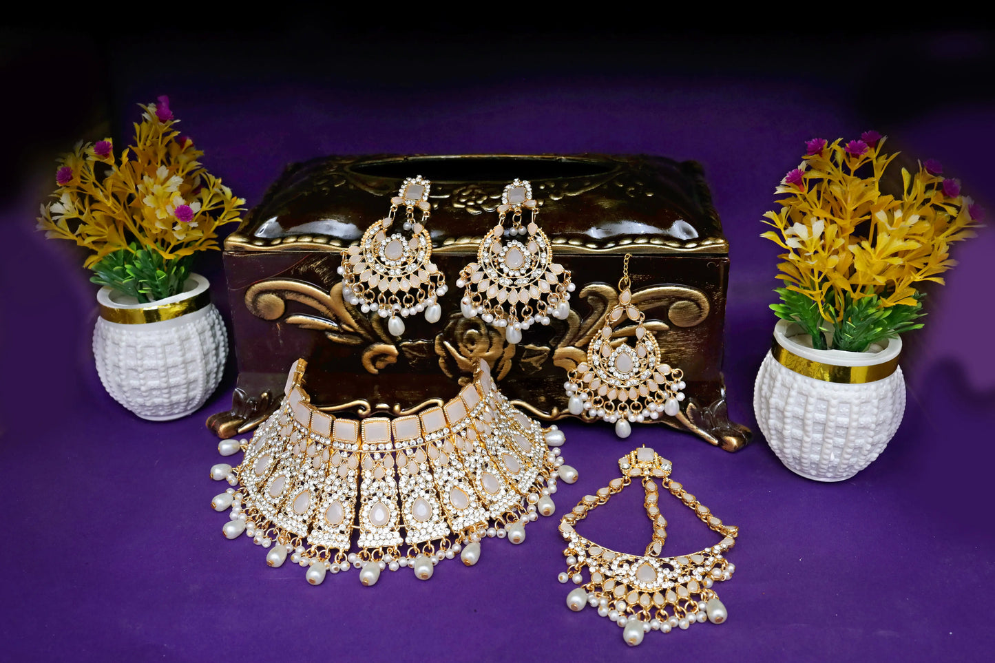 Set of gold and pearl jewelry on a purple background with decorative vases.