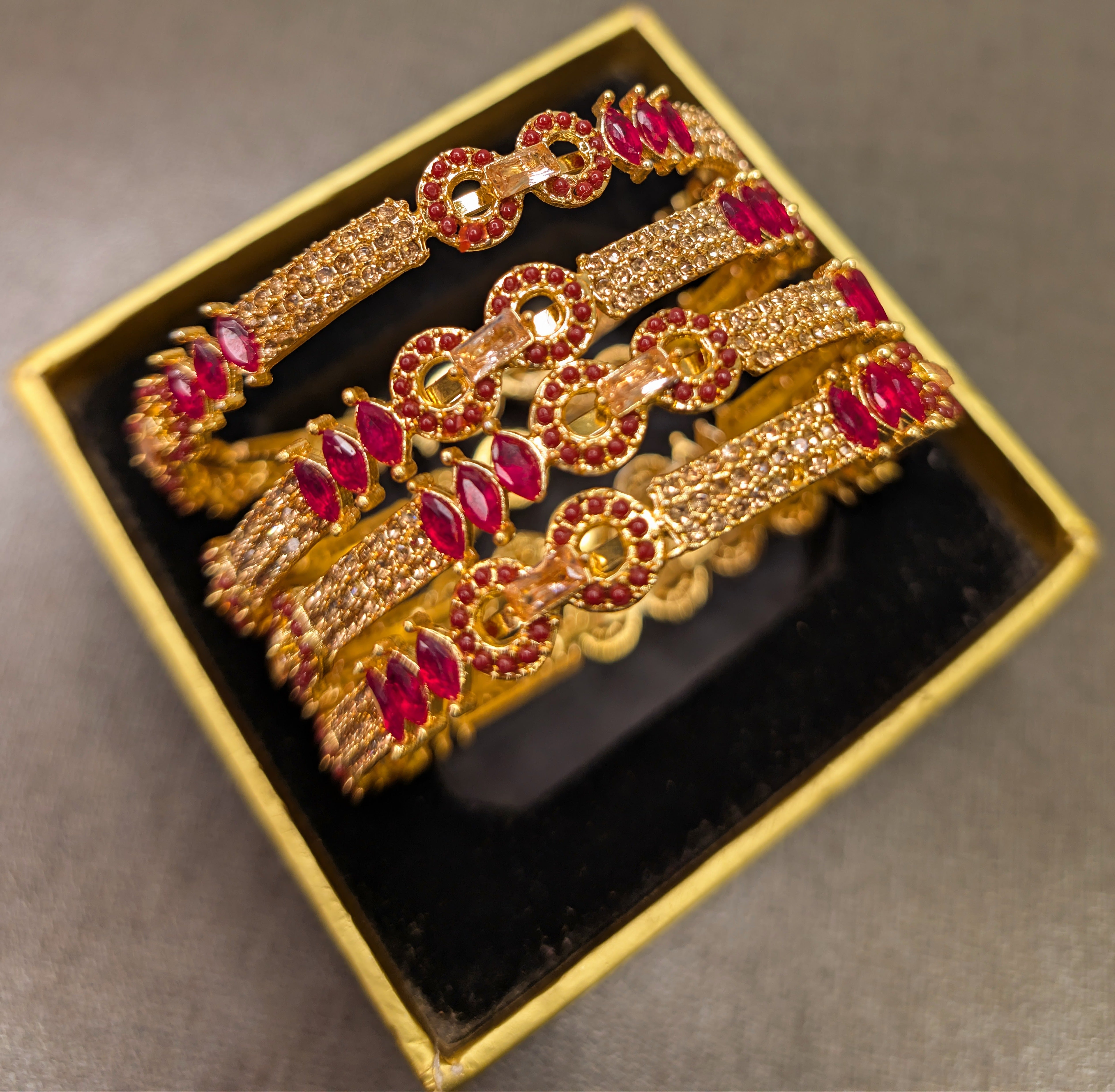 Set of gold and red gemstone bracelets in a box on a gray background